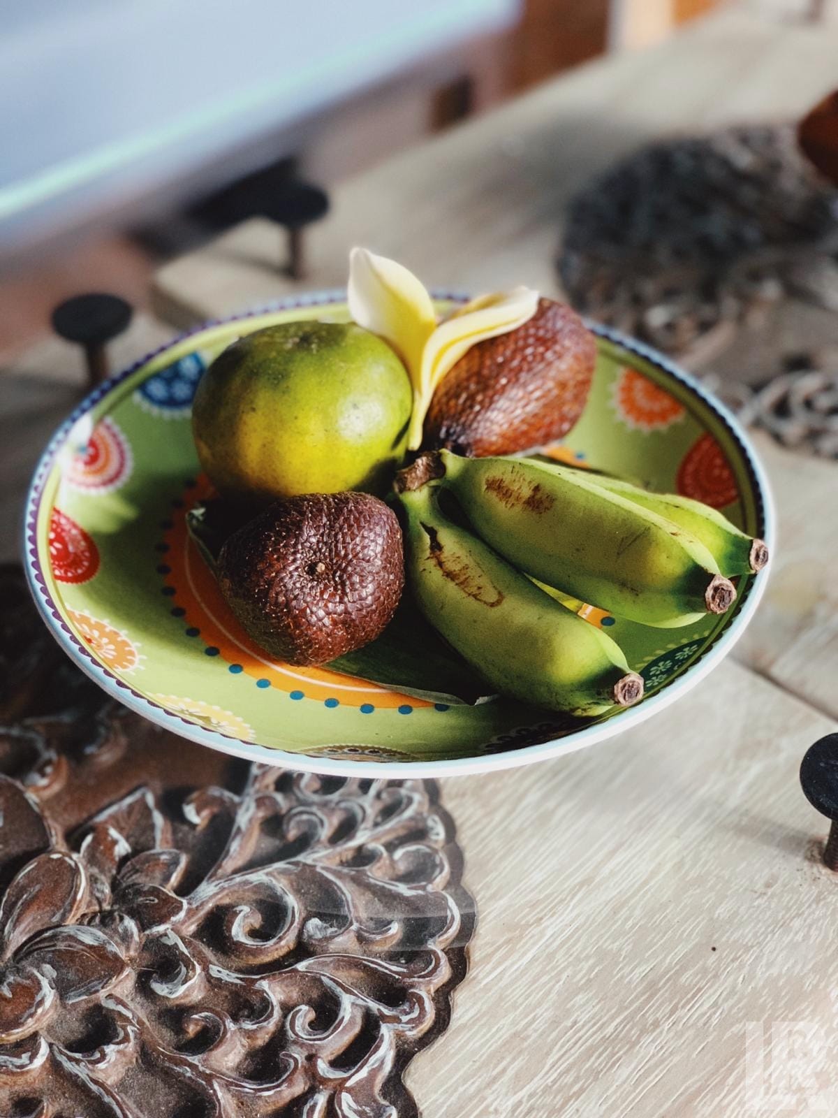 Colorful plate with green bananas, snake fruit, citrus, and a white flower on a wooden surface