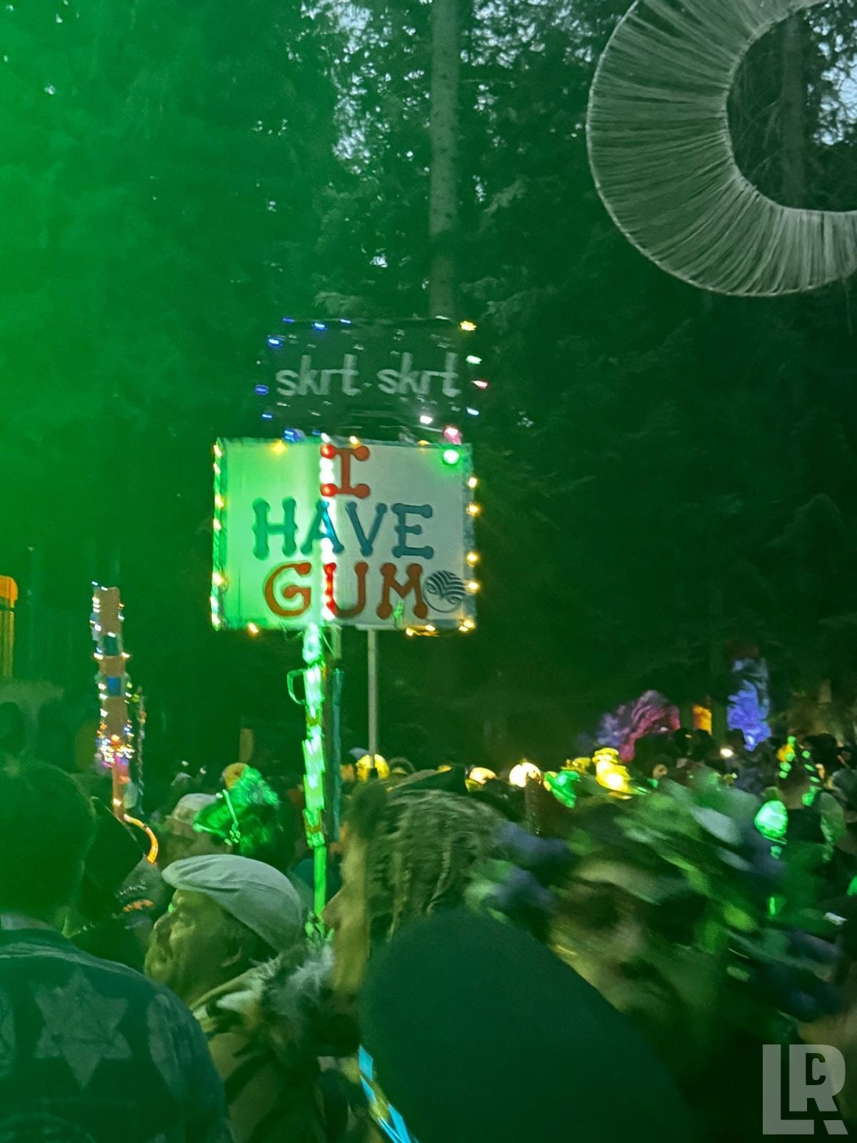 Light-decorated sign saying I Have Gum held above a crowd at a nighttime outdoor festival