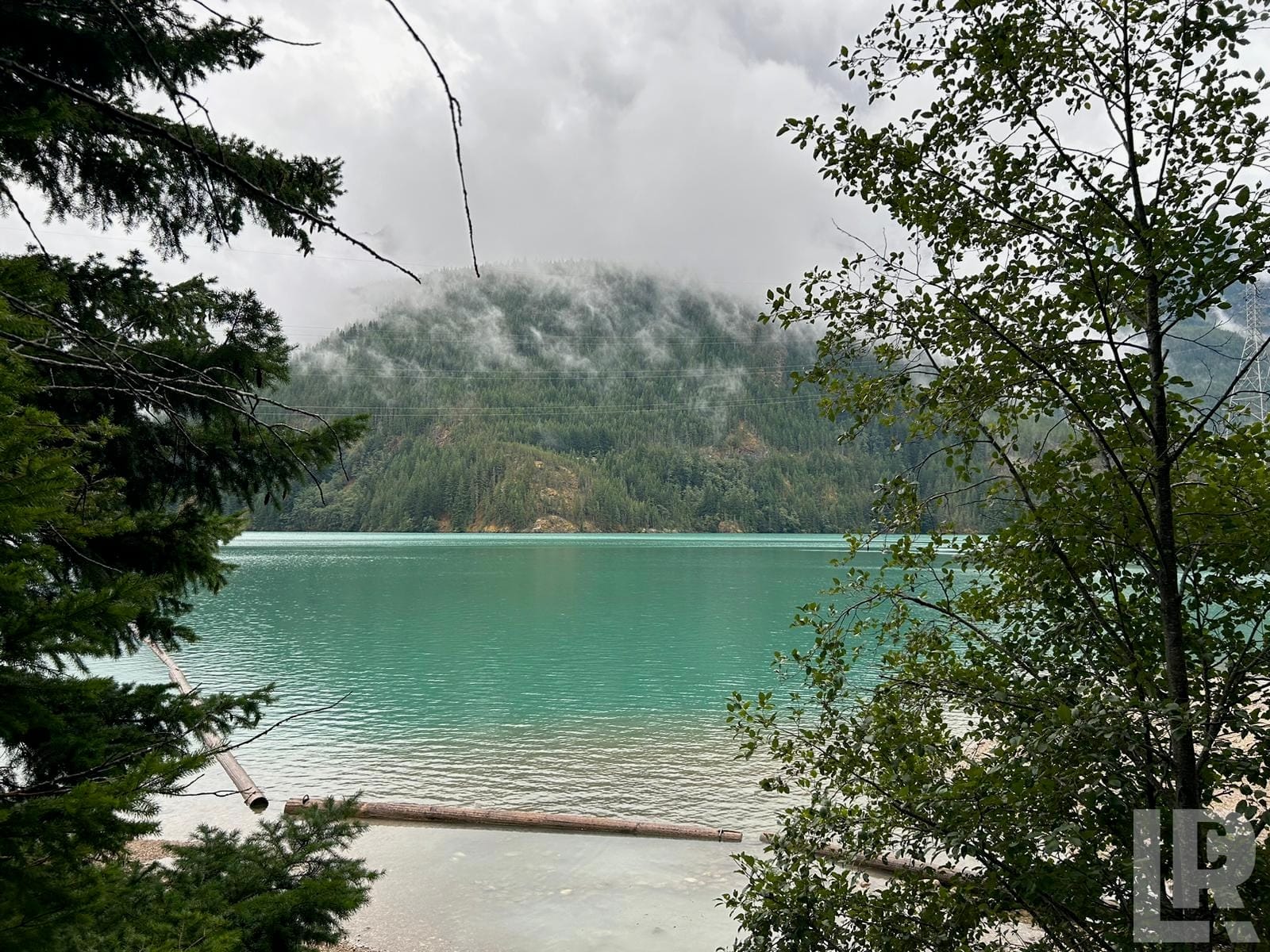Turquoise lake framed by trees with a misty forested mountain in the background