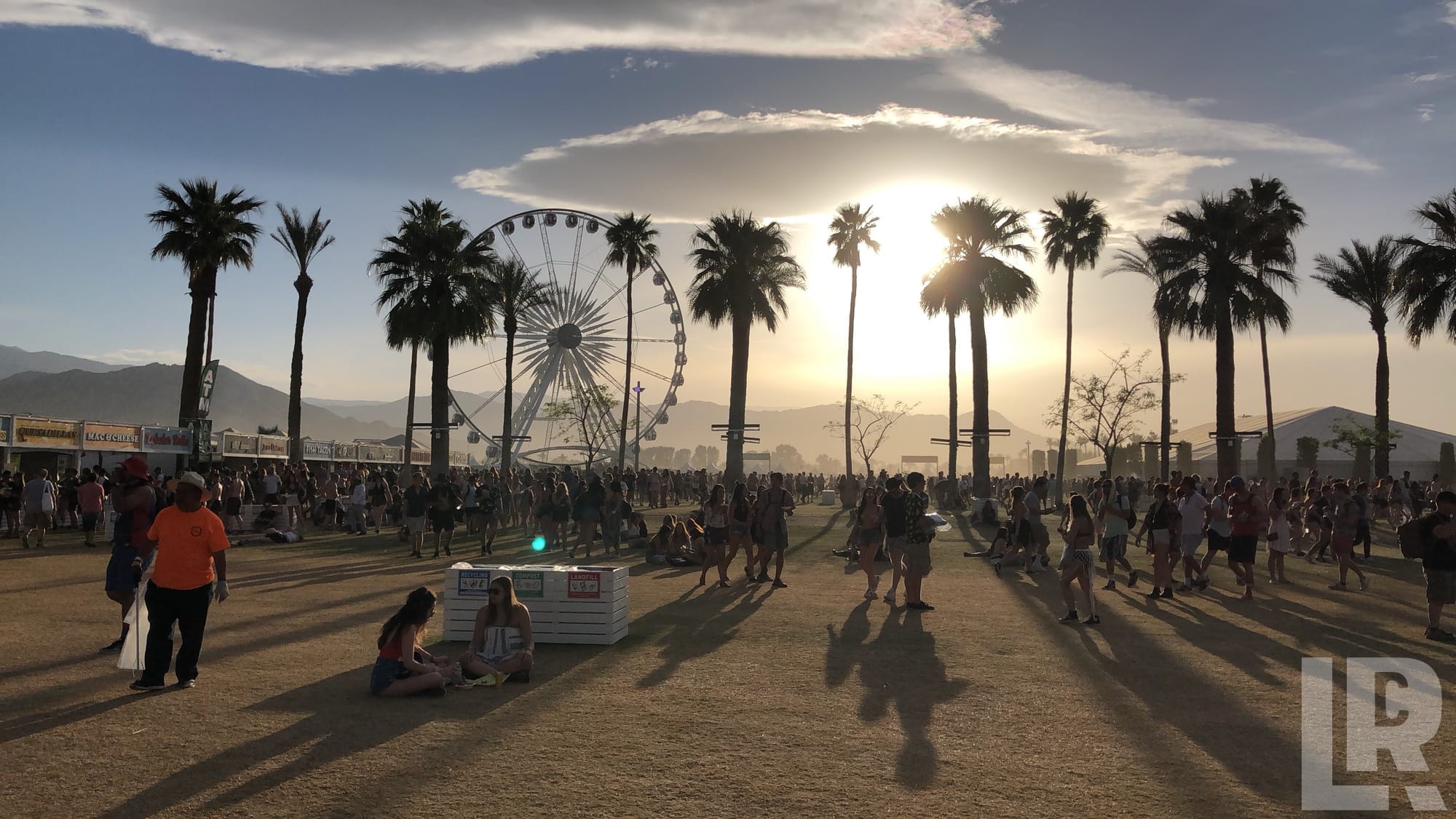 Festival crowd with palm trees and Ferris wheel at sunset