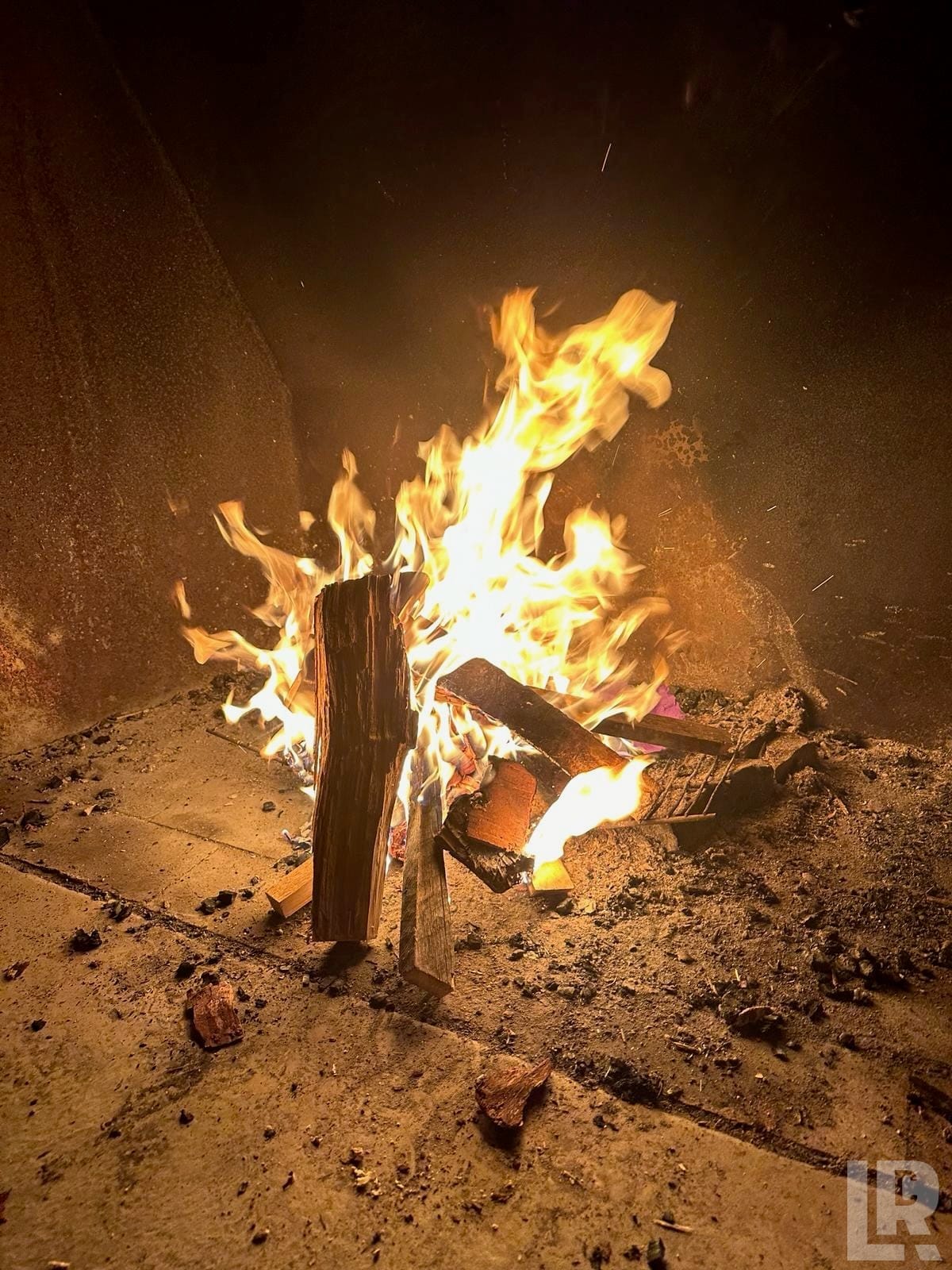 Bright wood fire with tall flames burning on a stone surface in a dark outdoor or indoor enclosure
