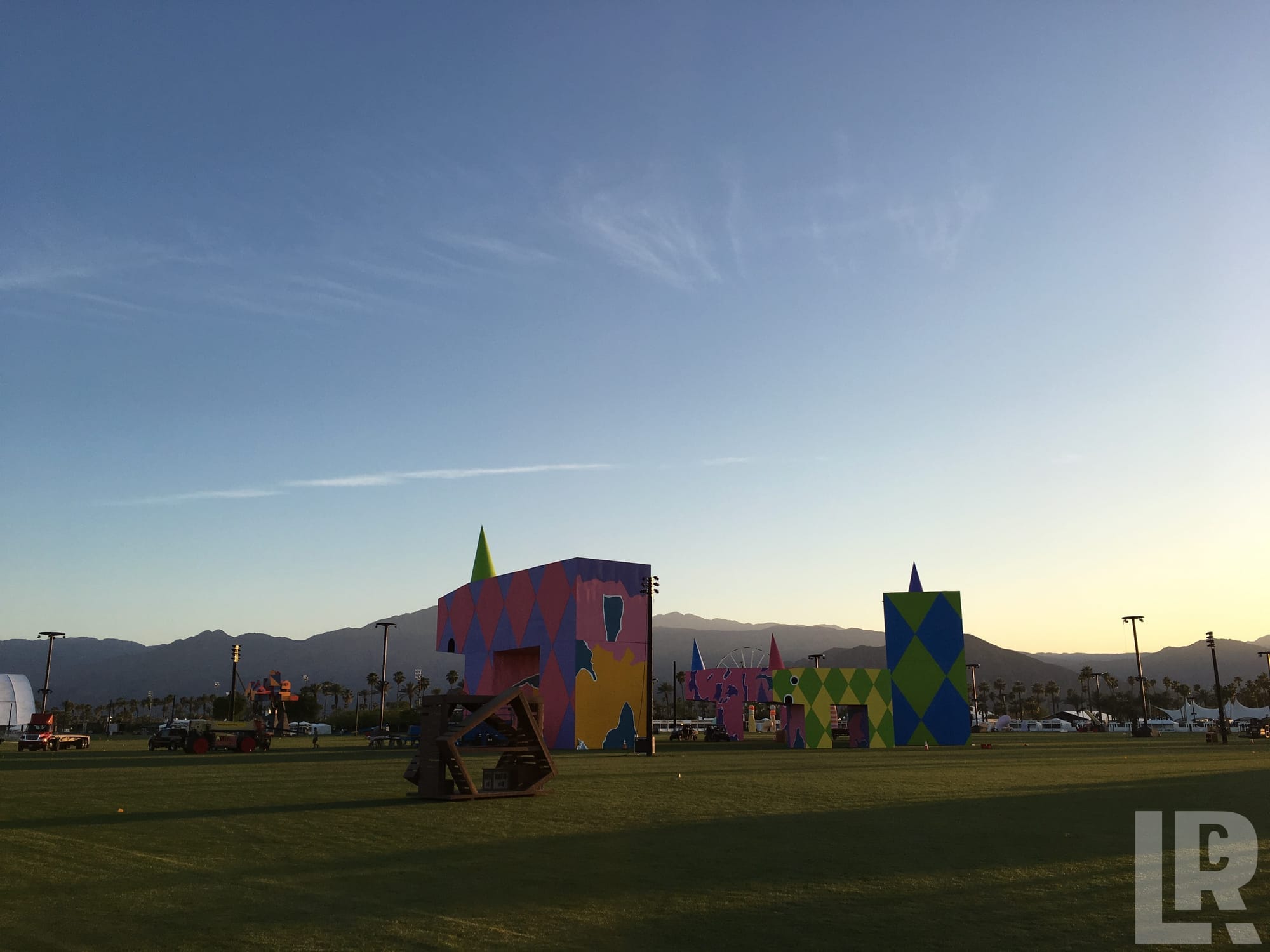 Large colorful geometric art structures on a grassy field at golden hour with mountain backdrop