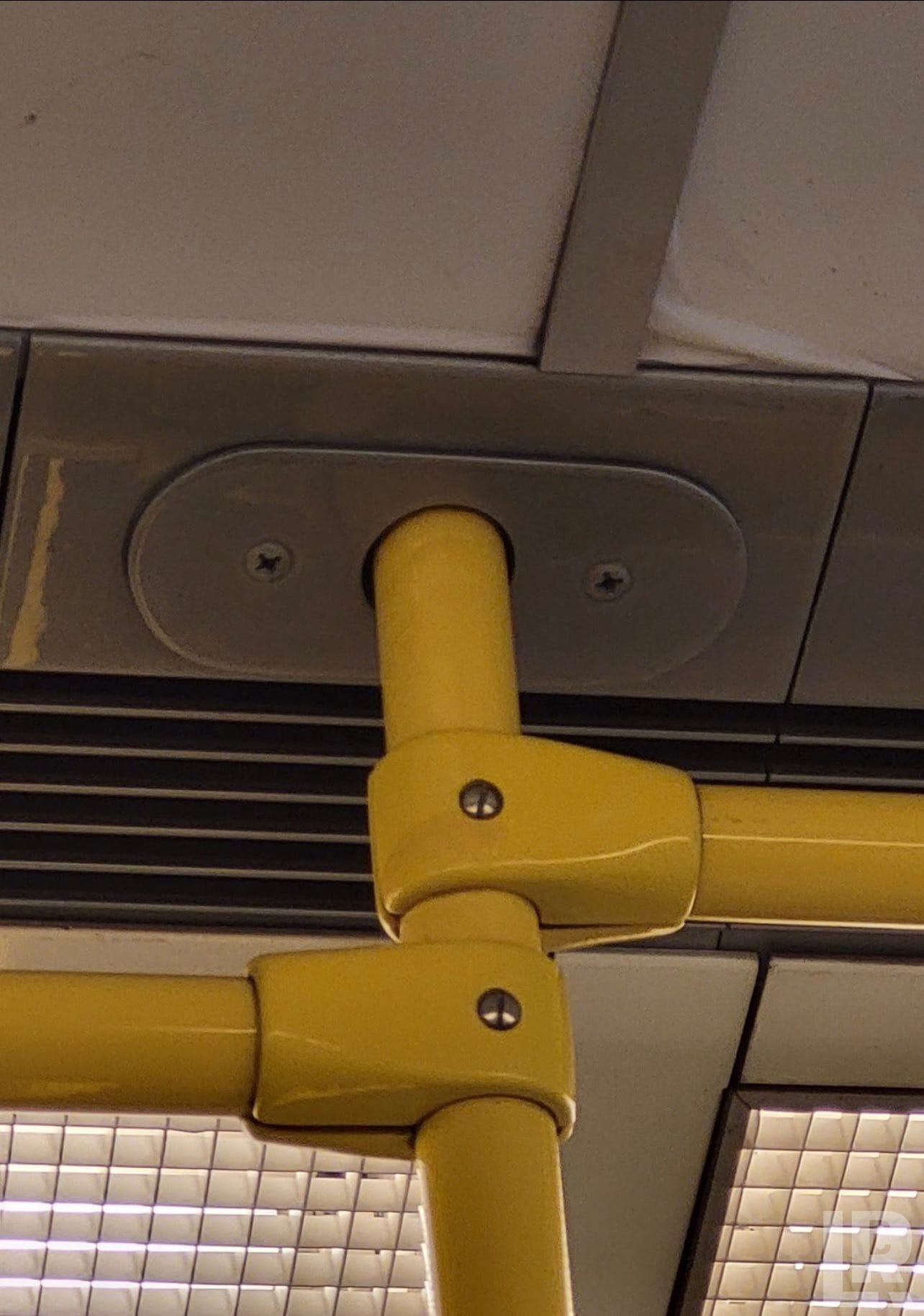 Yellow handrail pole connector mounted to the ceiling of a bus or train car