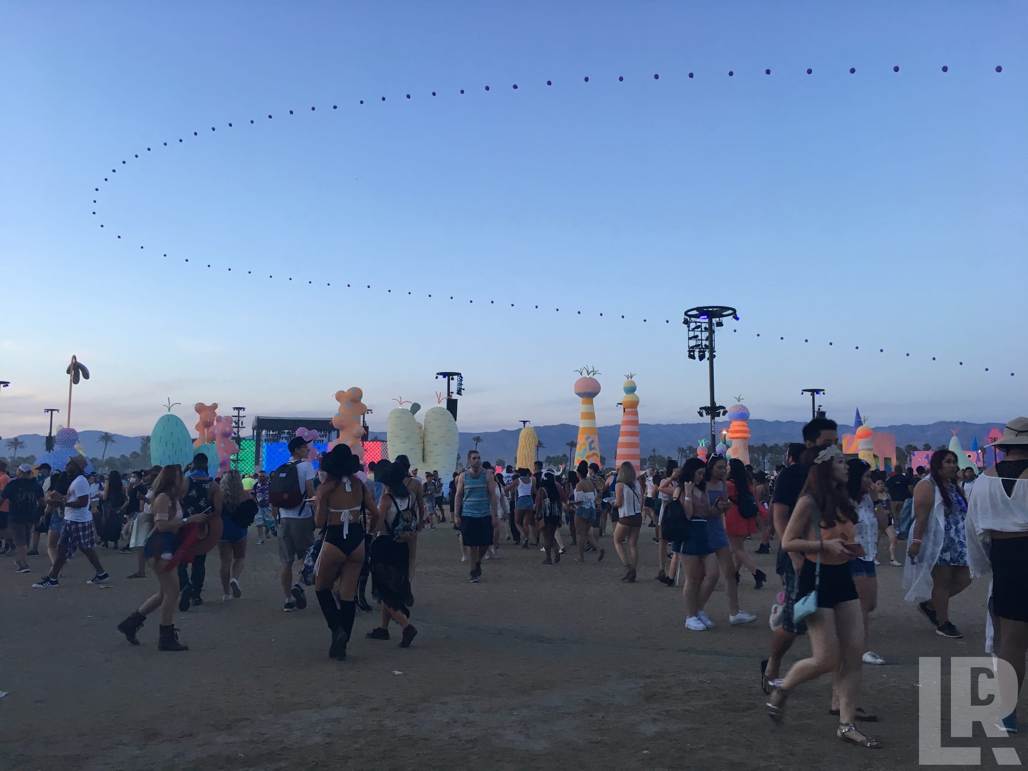Crowd at an outdoor music festival with colorful inflatable art installations at twilight