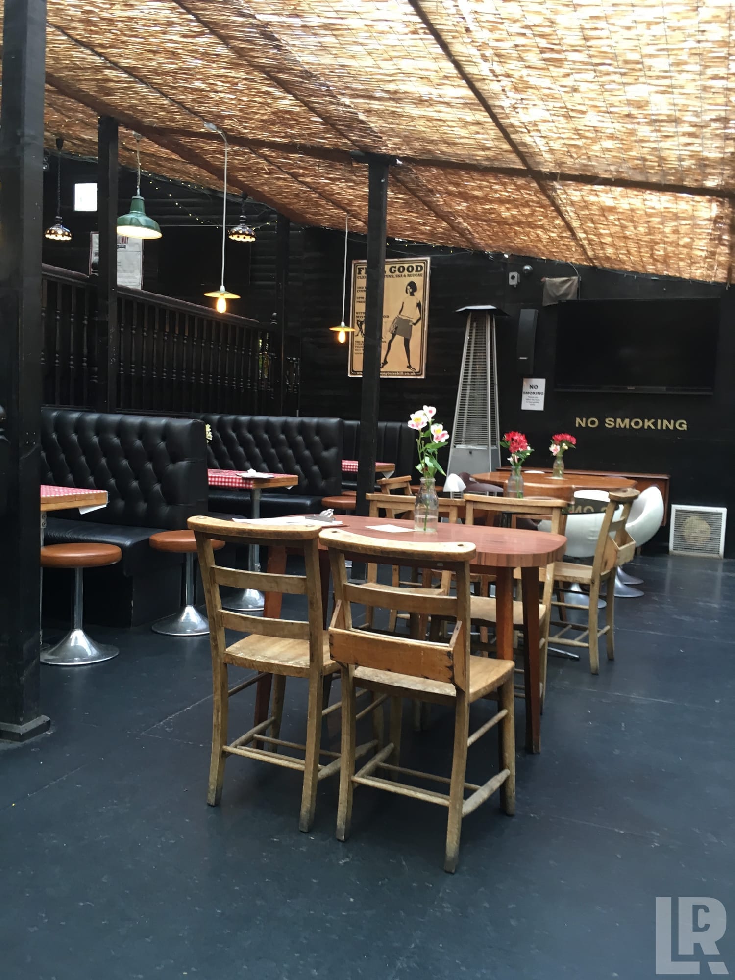 Empty bar interior with wooden bar stools, black leather booth seating, pendant lights, and a straw thatched ceiling