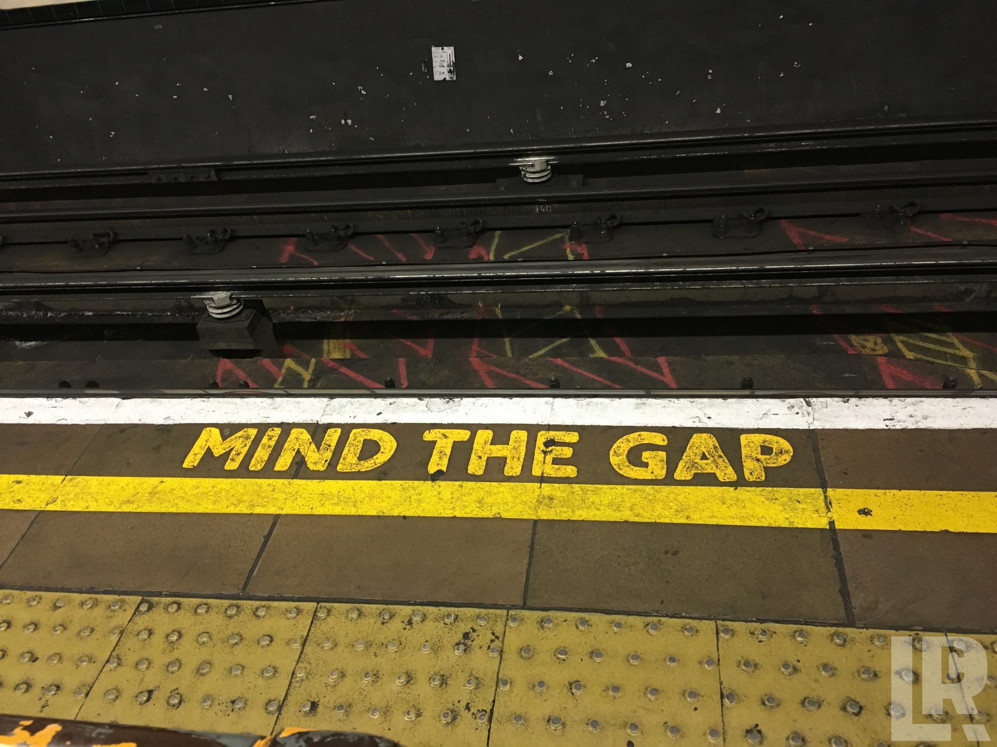 Yellow Mind the Gap text painted on a subway platform floor next to railway tracks