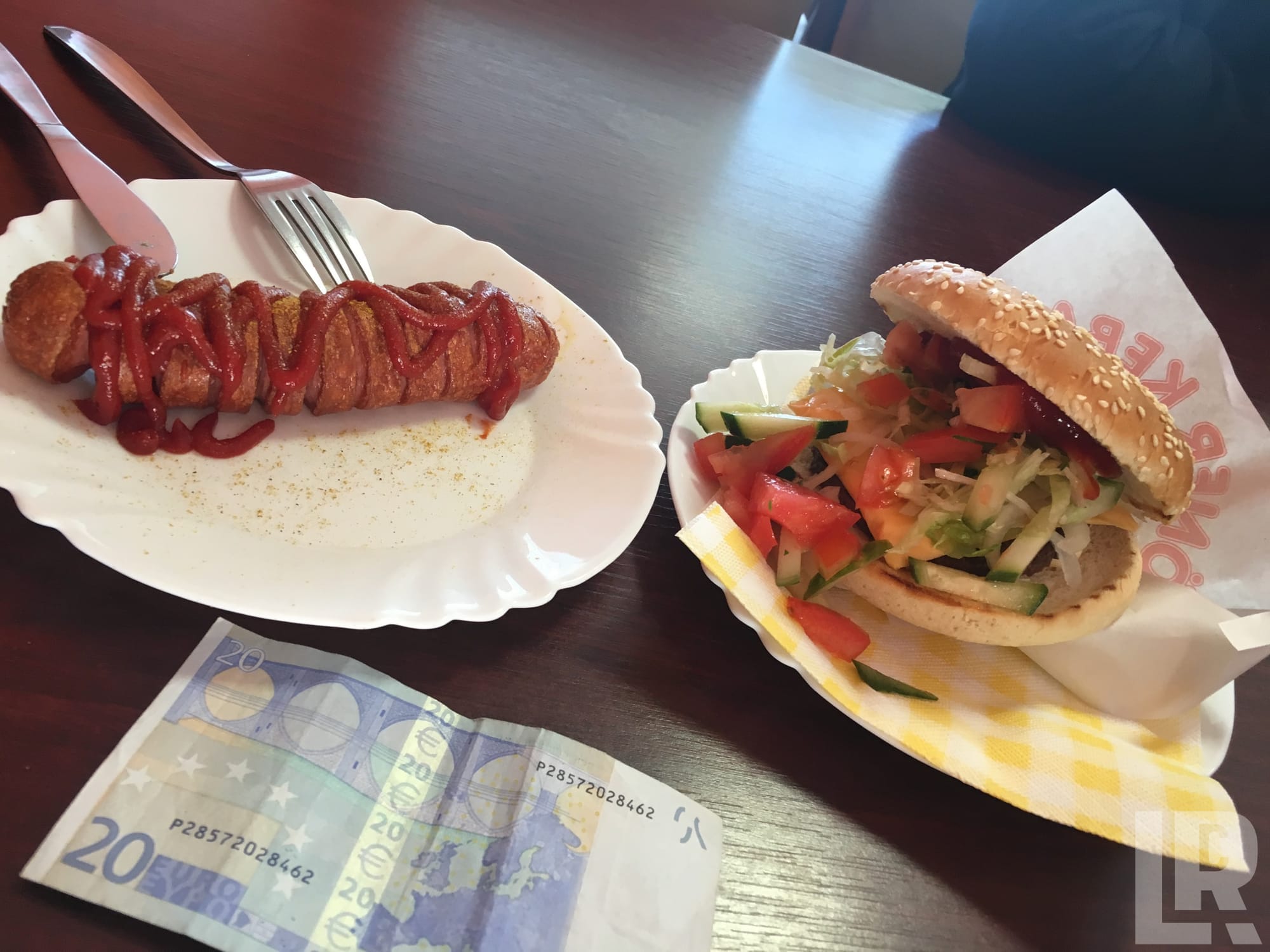 Currywurst and kebab burger with vegetables on a dark wooden table with a 20 euro note