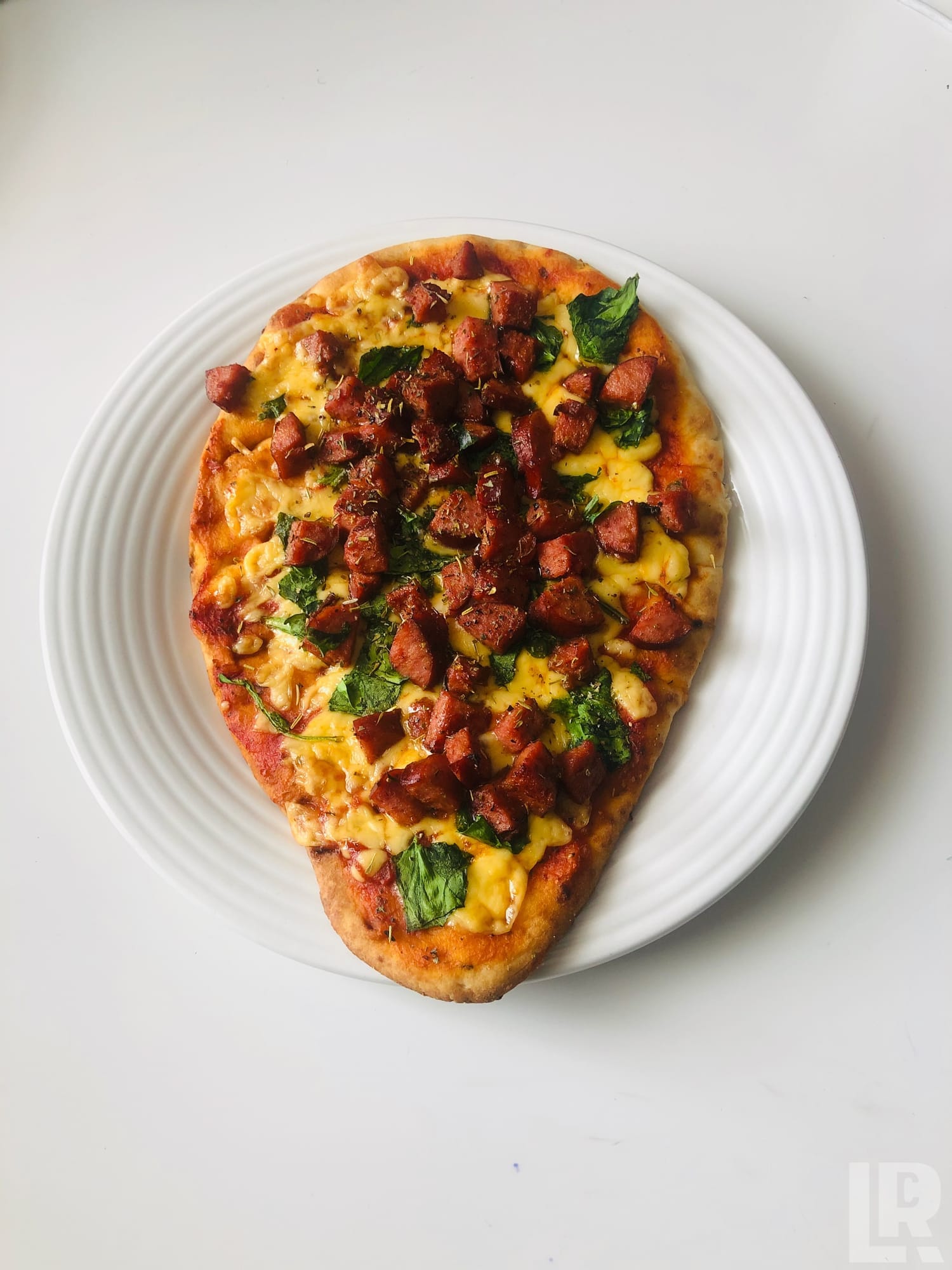 Flatbread pizza with cheese, sausage, and spinach on a white plate