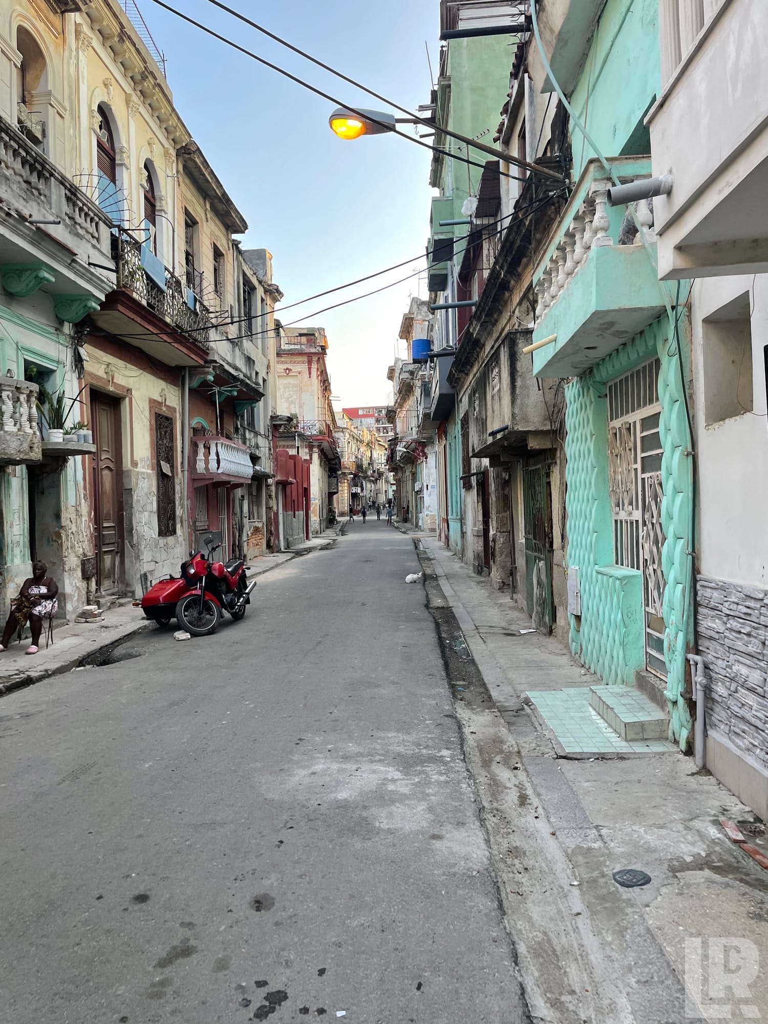 Narrow street with aging pastel colonial buildings, a red sidecar motorcycle, and an illuminated street lamp