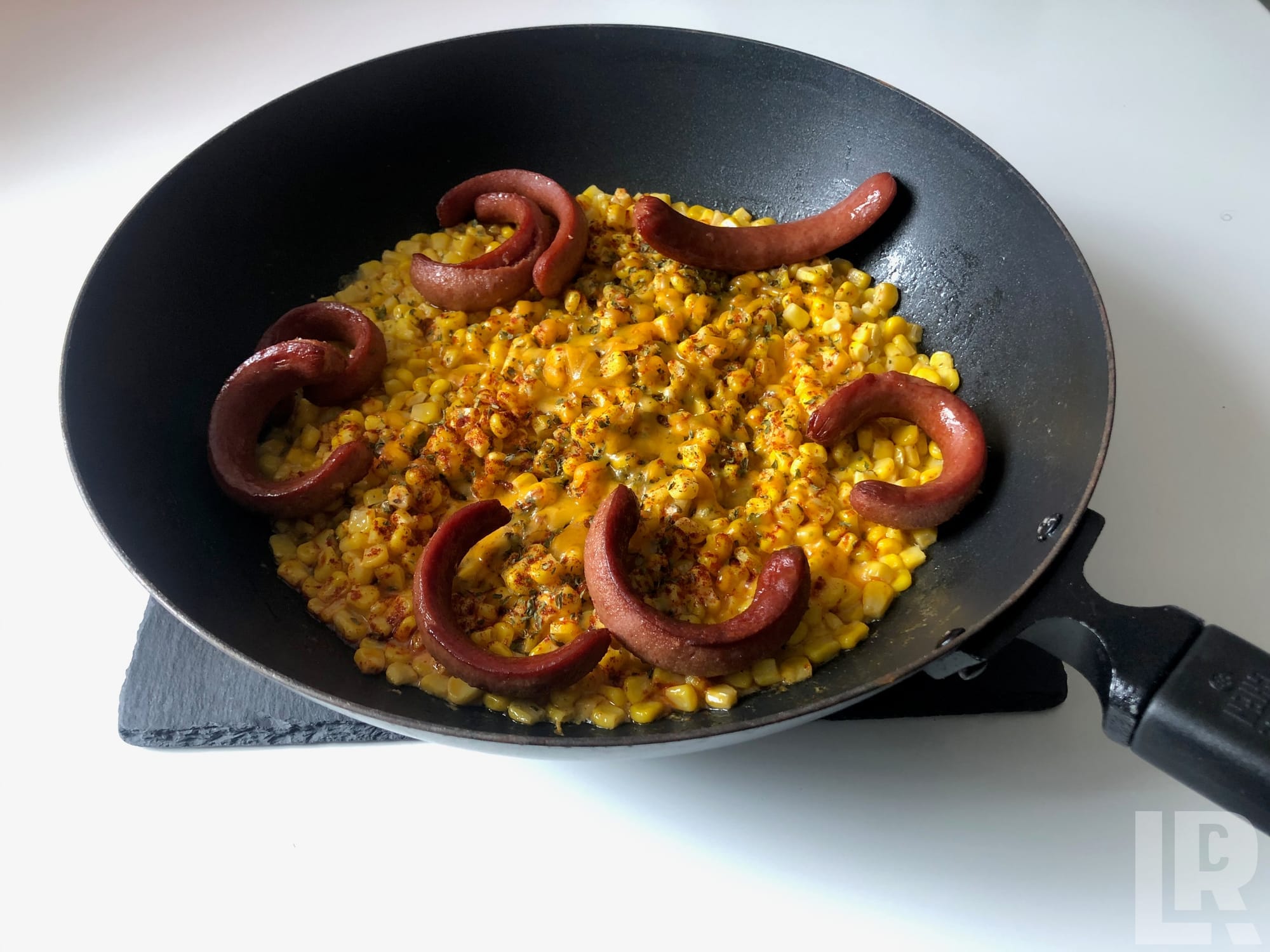 Frying pan with seasoned corn and curled cocktail sausages