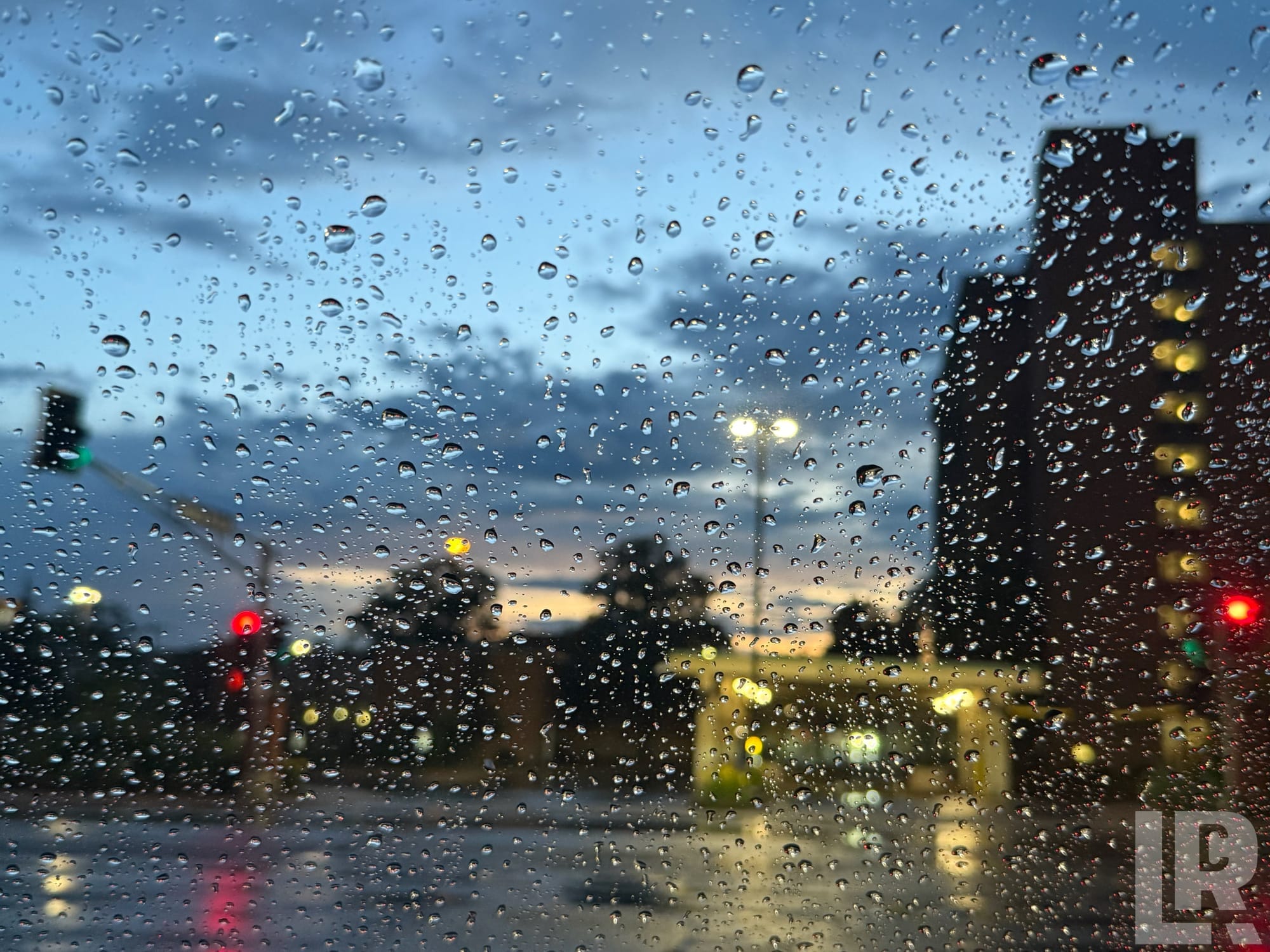 View through a rain-covered windshield of a city street at dusk with colorful blurred traffic lights