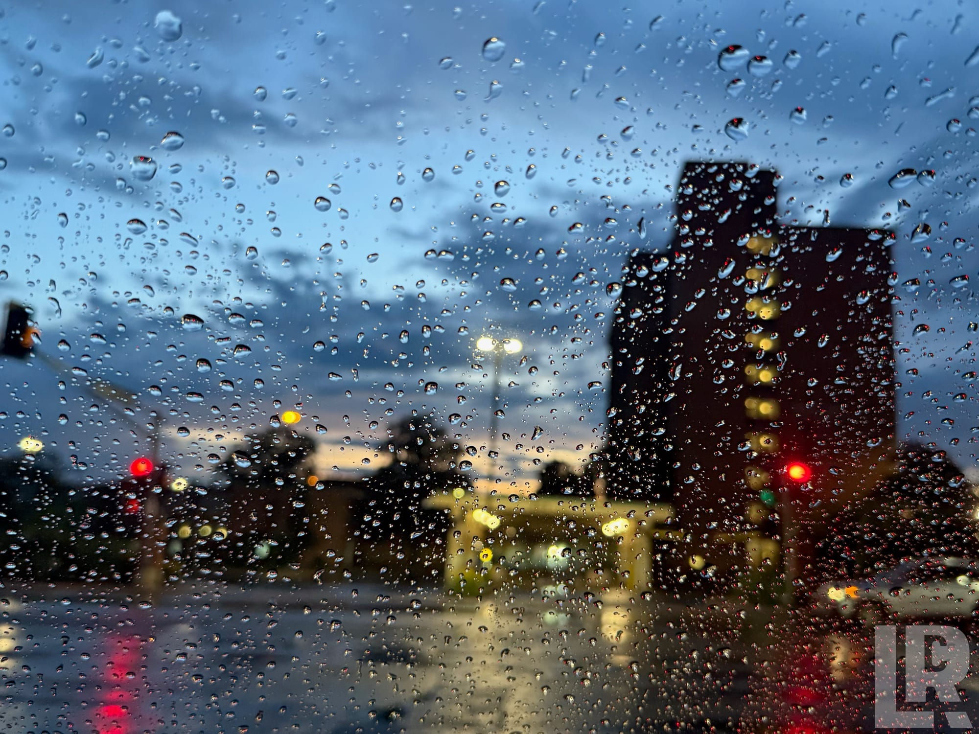 View through a wet windshield of a rainy city intersection at dusk with red traffic lights and glowing street lamps