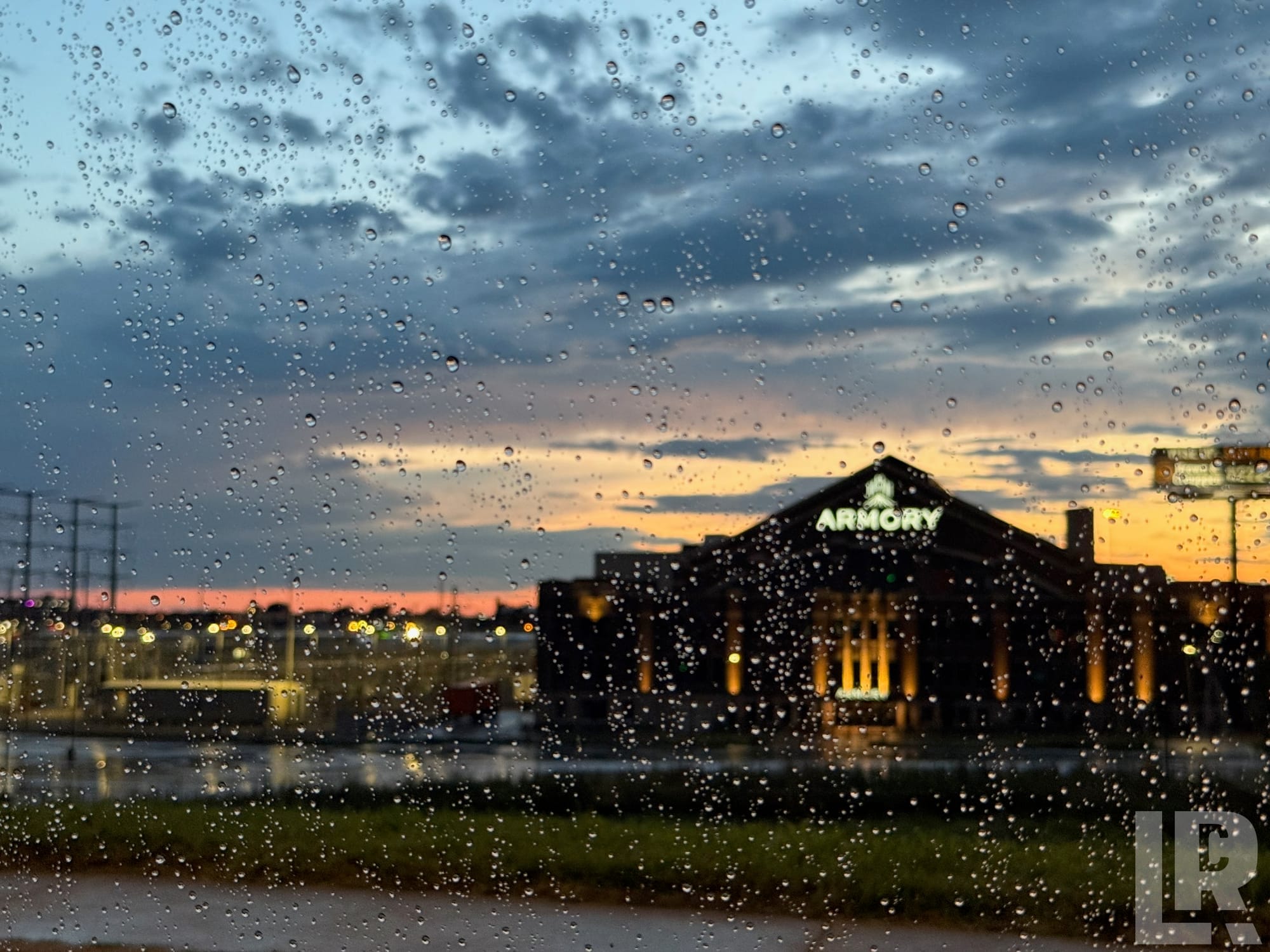 Rain droplets on a window with a glowing Armory building and sunset sky in the background