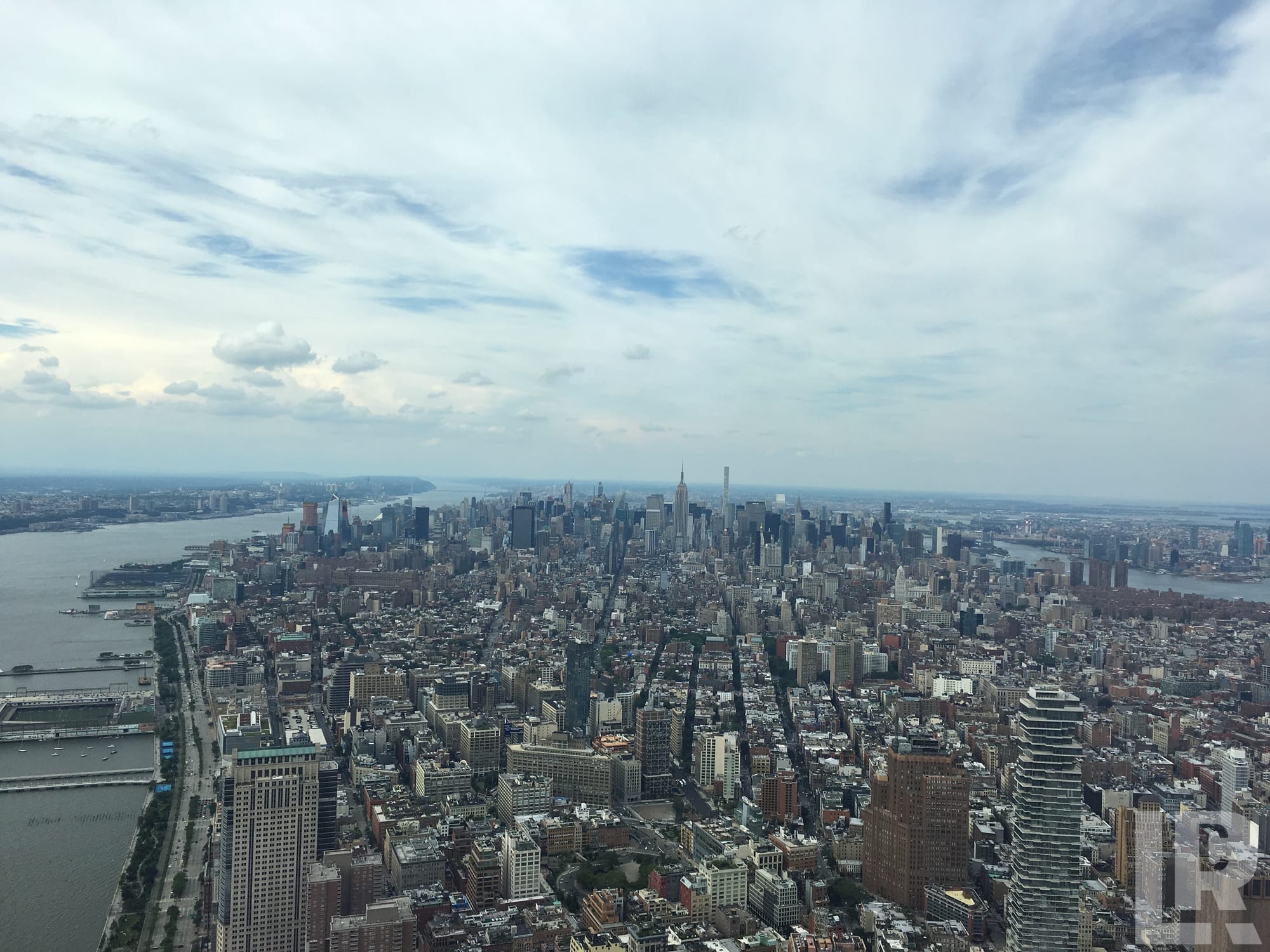 Aerial panoramic view of a large city skyline with rivers on either side under a cloudy sky