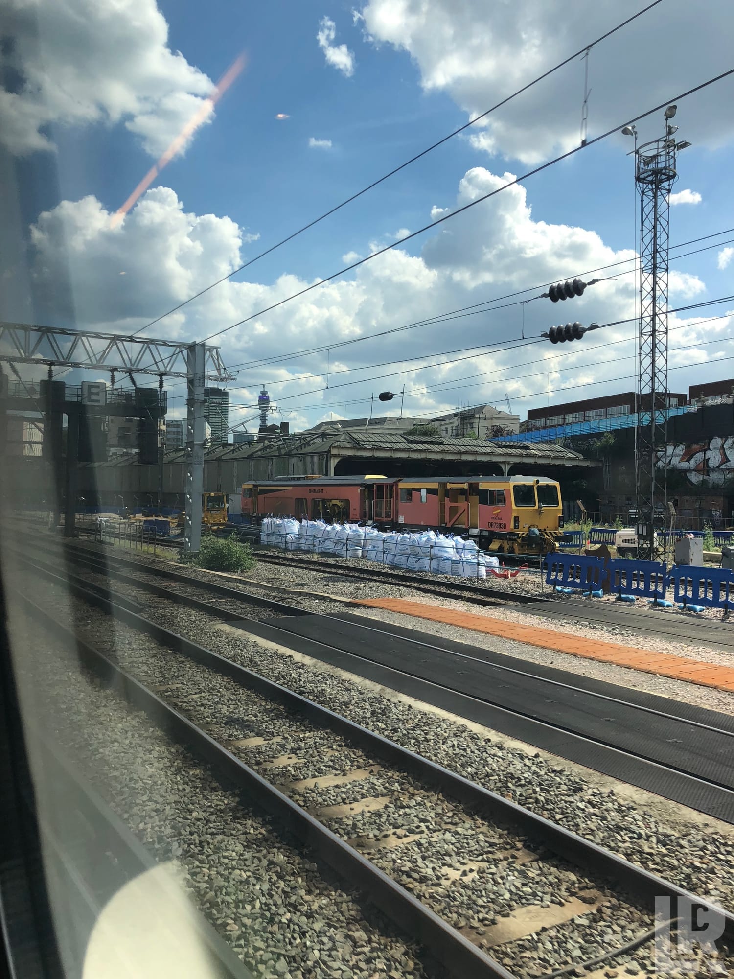 Railway maintenance tamper machine and ballast bags seen from a passing train window