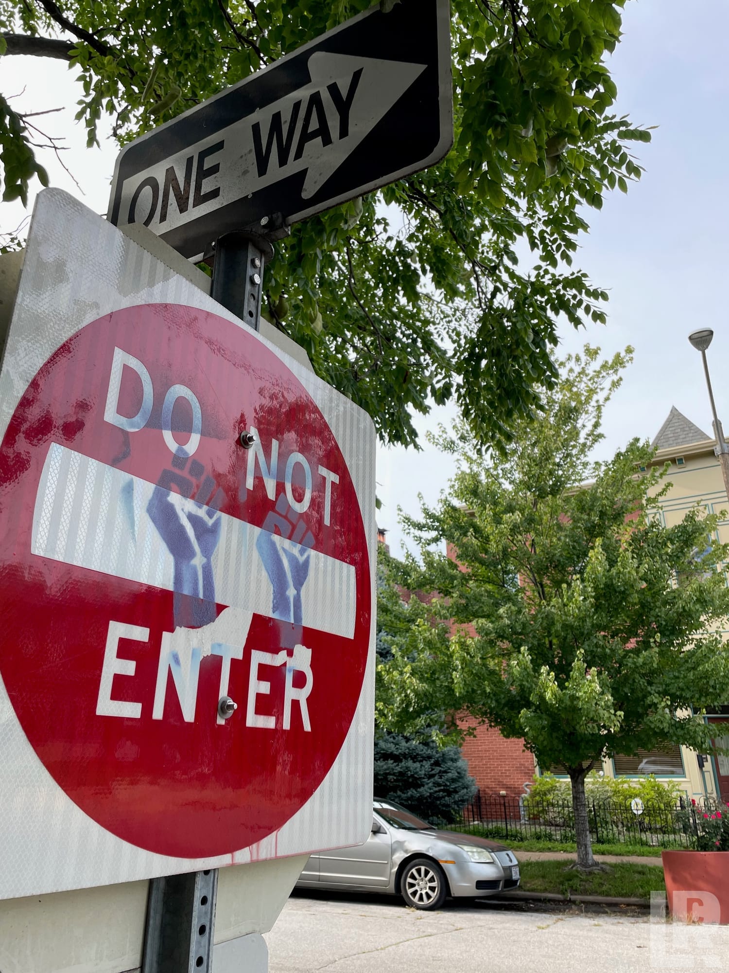 Do Not Enter sign with raised fist stickers below a One Way sign on a city street