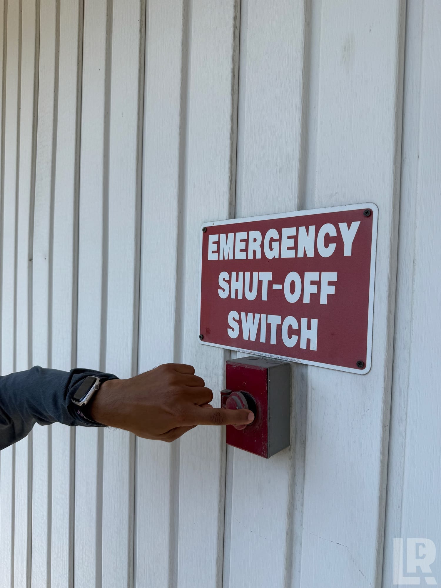 Hand pressing a red emergency shut-off switch on a white metal wall