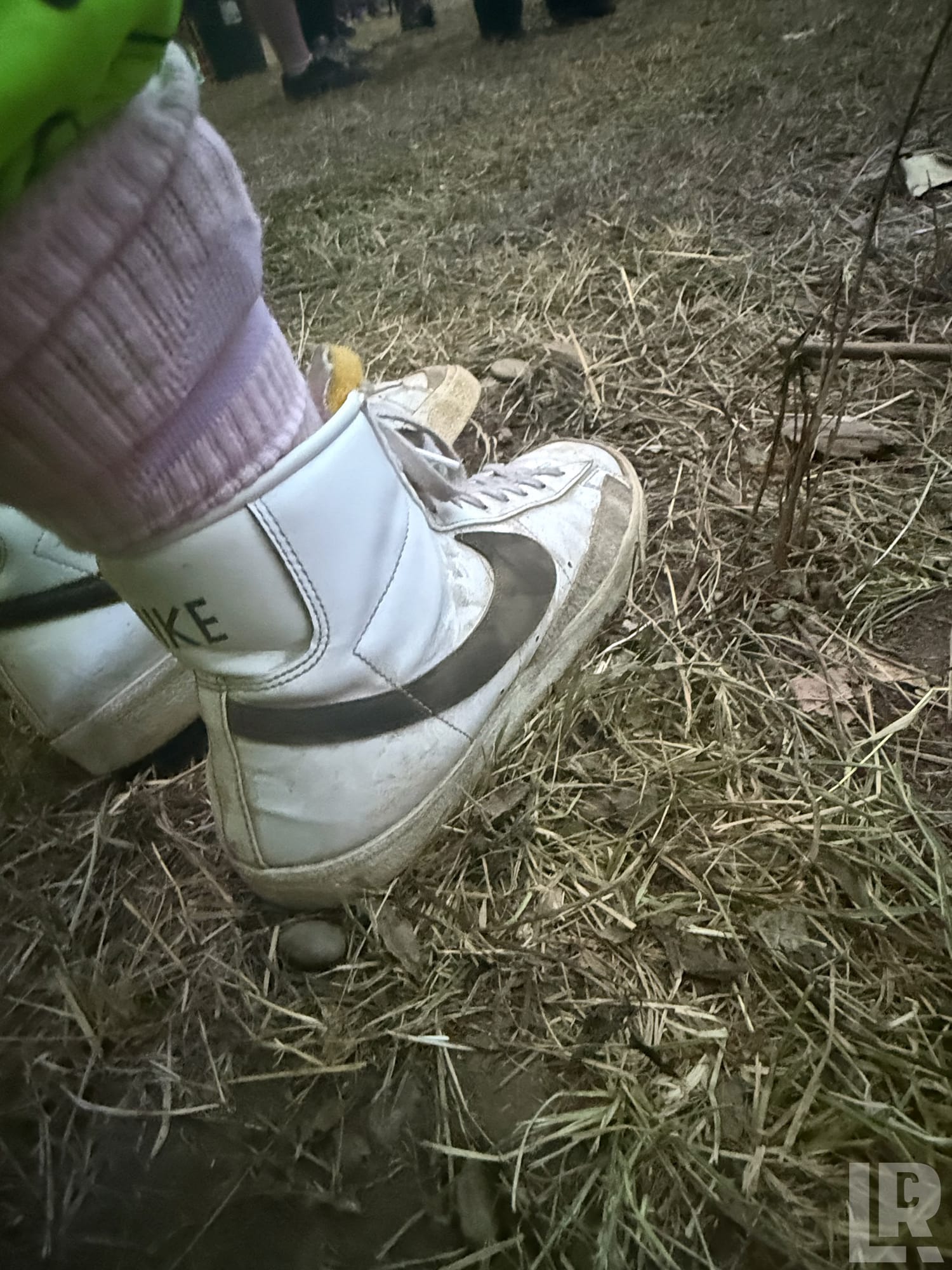 Close-up of a dirty white Nike high-top sneaker with pink sock on dry grass