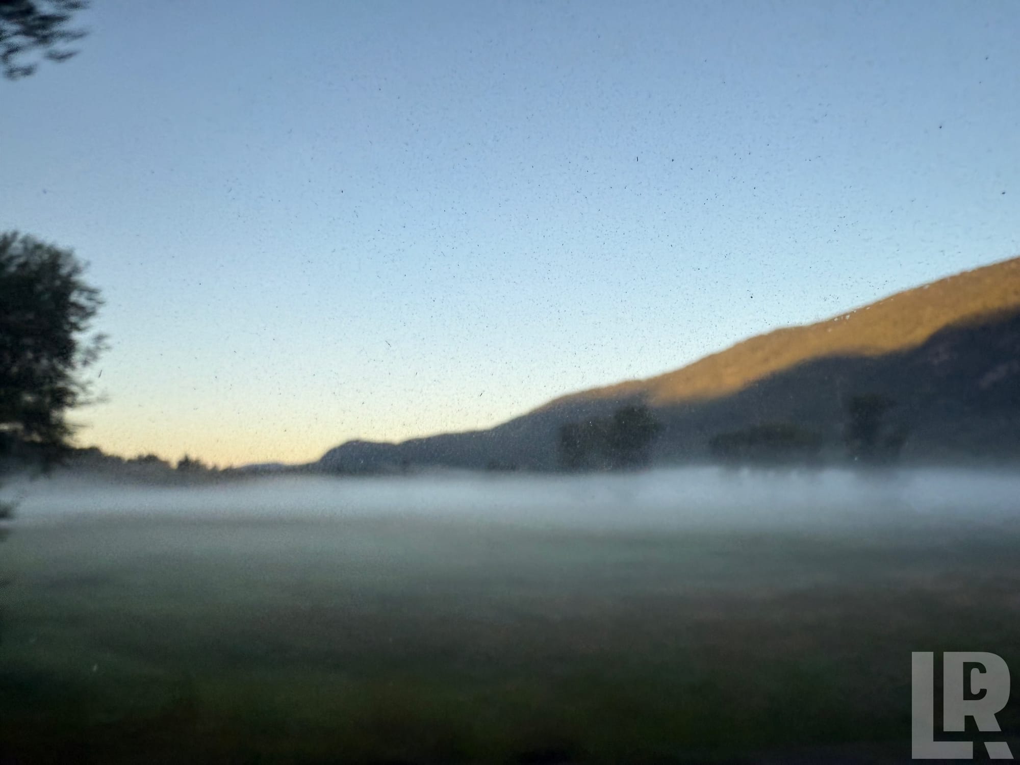 Low morning fog over a green valley with hills and a pastel sunrise sky