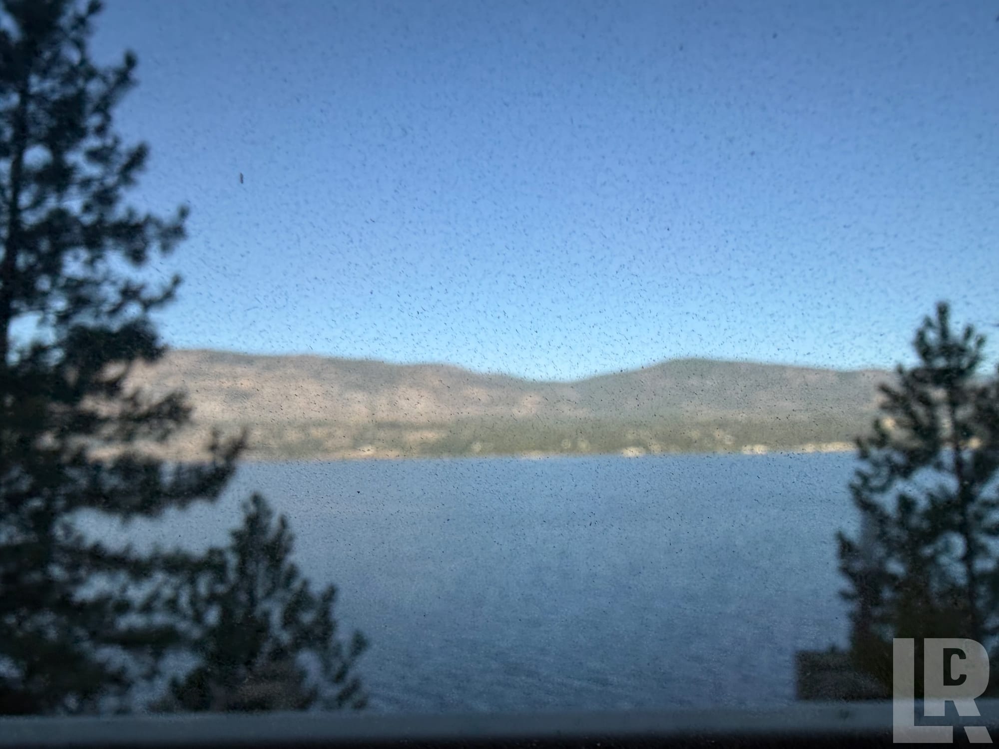 Lake and hills seen through a dusty window with pine trees on either side