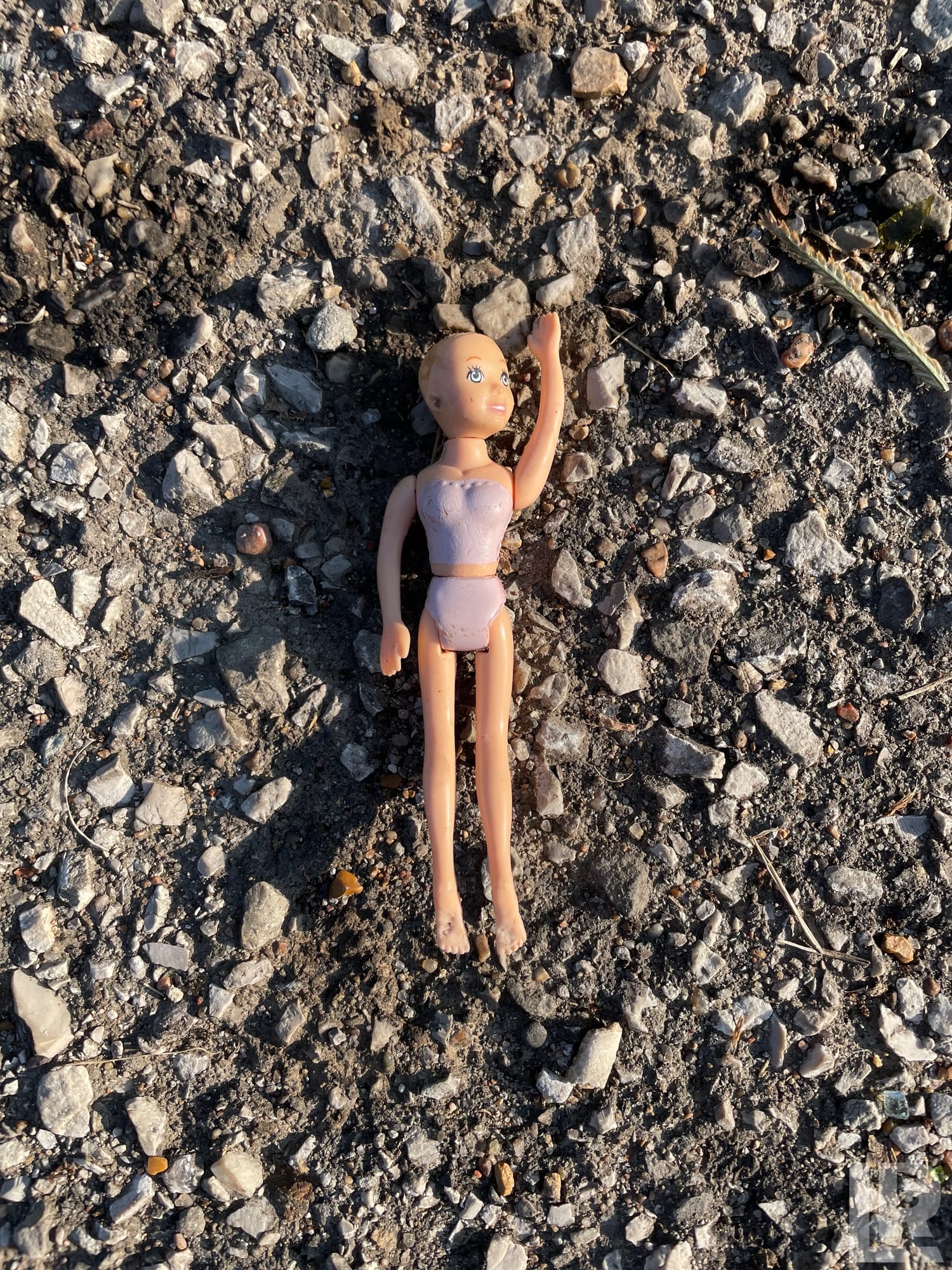 Dirty abandoned plastic doll lying on gravel ground