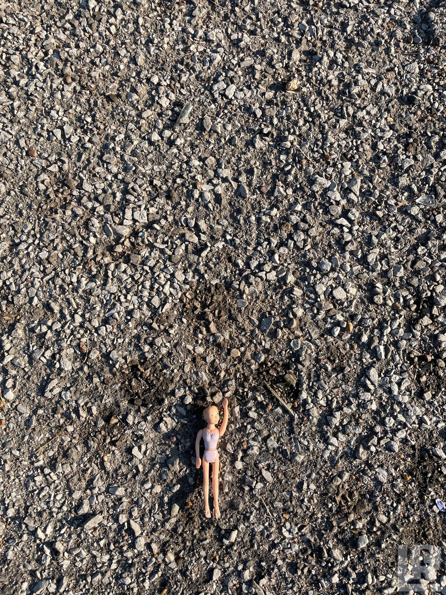 Discarded plastic fashion doll lying on gravel with one arm up