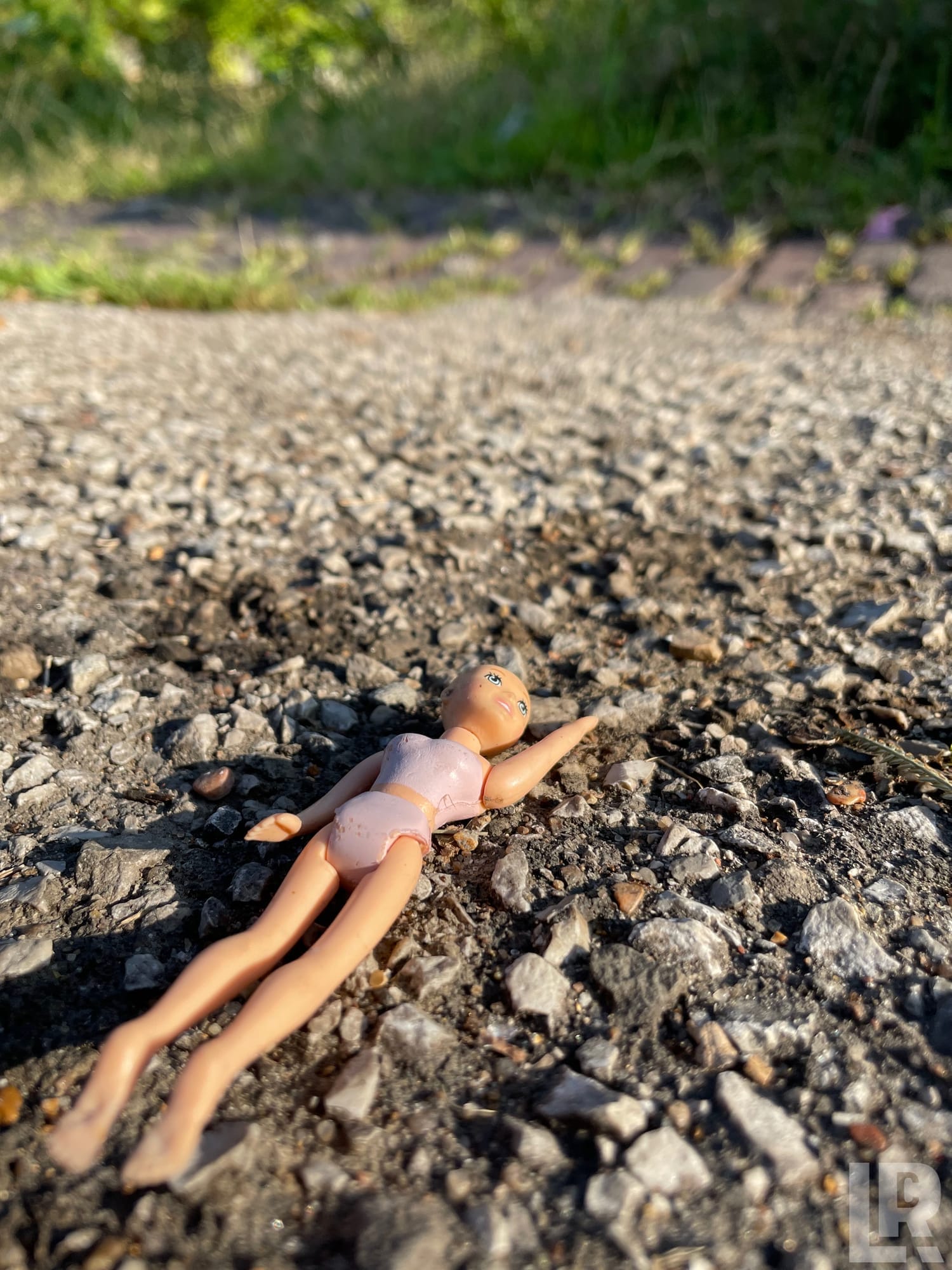 Abandoned plastic doll lying face-up on gravel ground