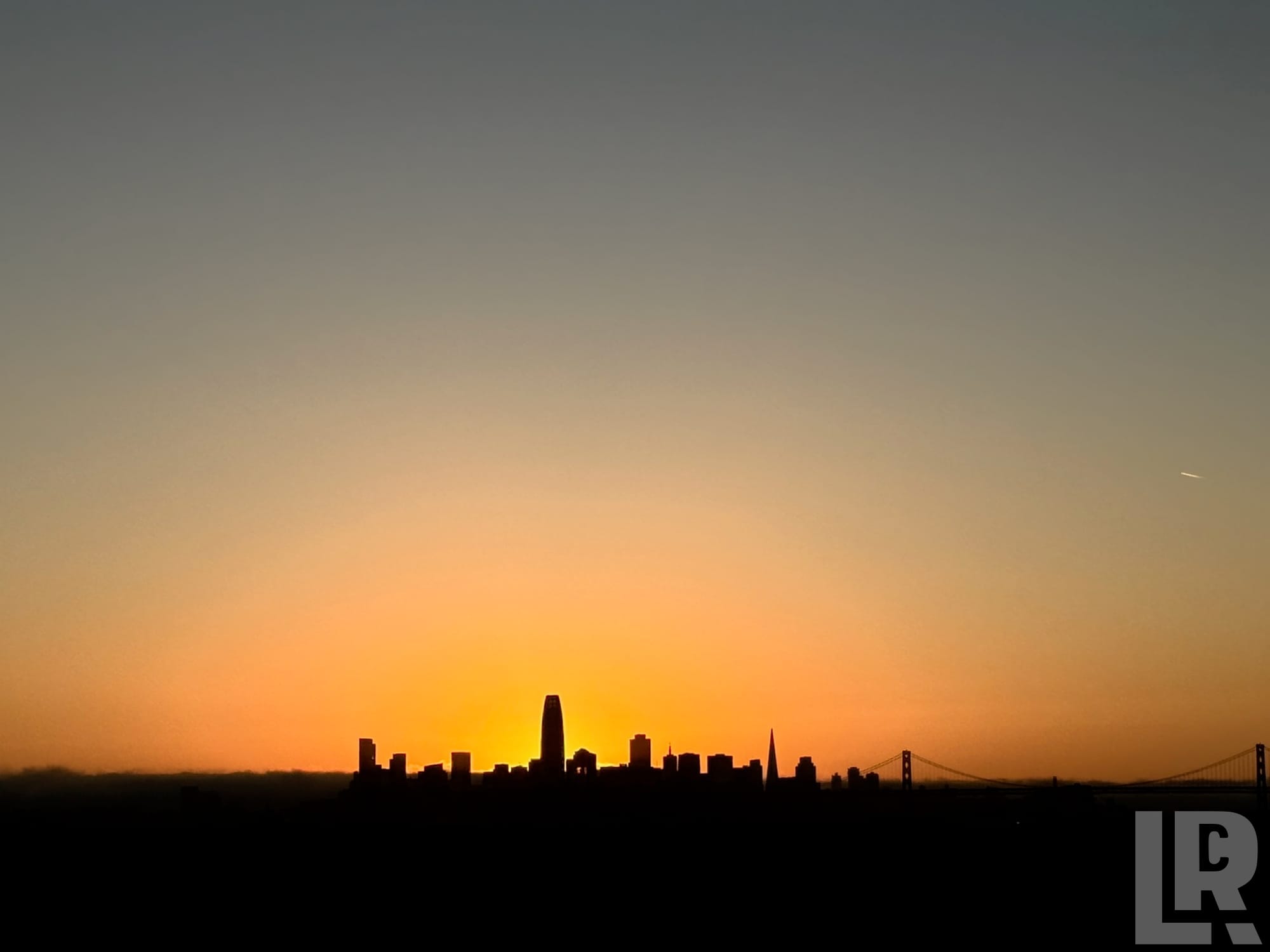 City skyline silhouette at sunset with orange sky and suspension bridge