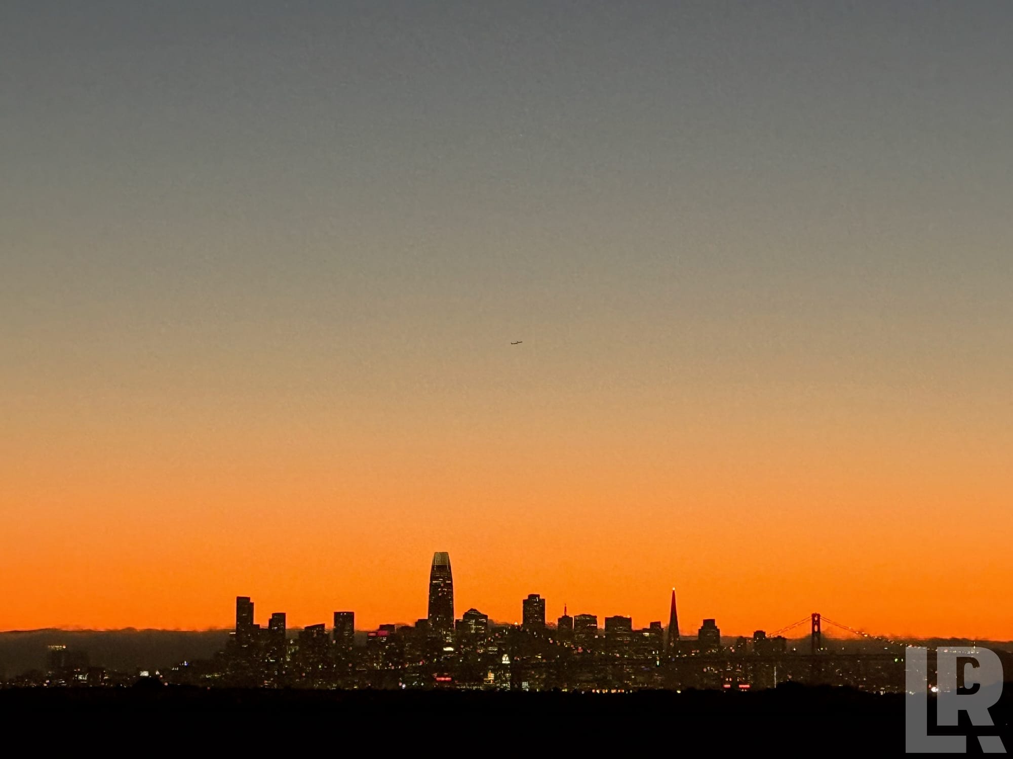City skyline silhouette at sunset with orange sky and suspension bridge
