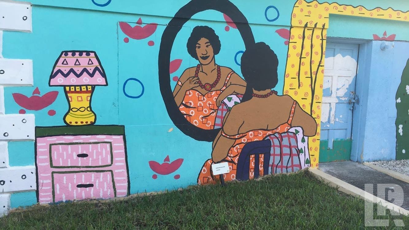 Vibrant wall mural of a woman looking at her reflection in a mirror with a lamp and dresser on a turquoise background