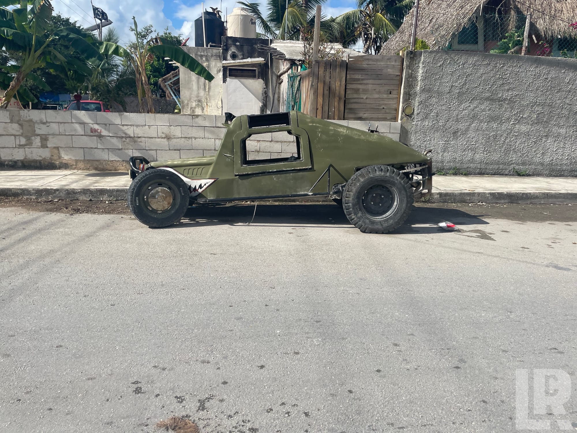 Green custom off-road buggy parked on a street next to a concrete wall