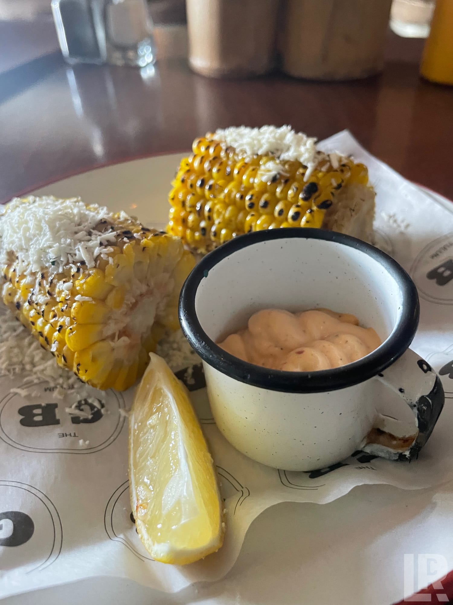 Grilled corn on the cob with cheese, a lemon wedge, and a cup of dipping sauce on a plate