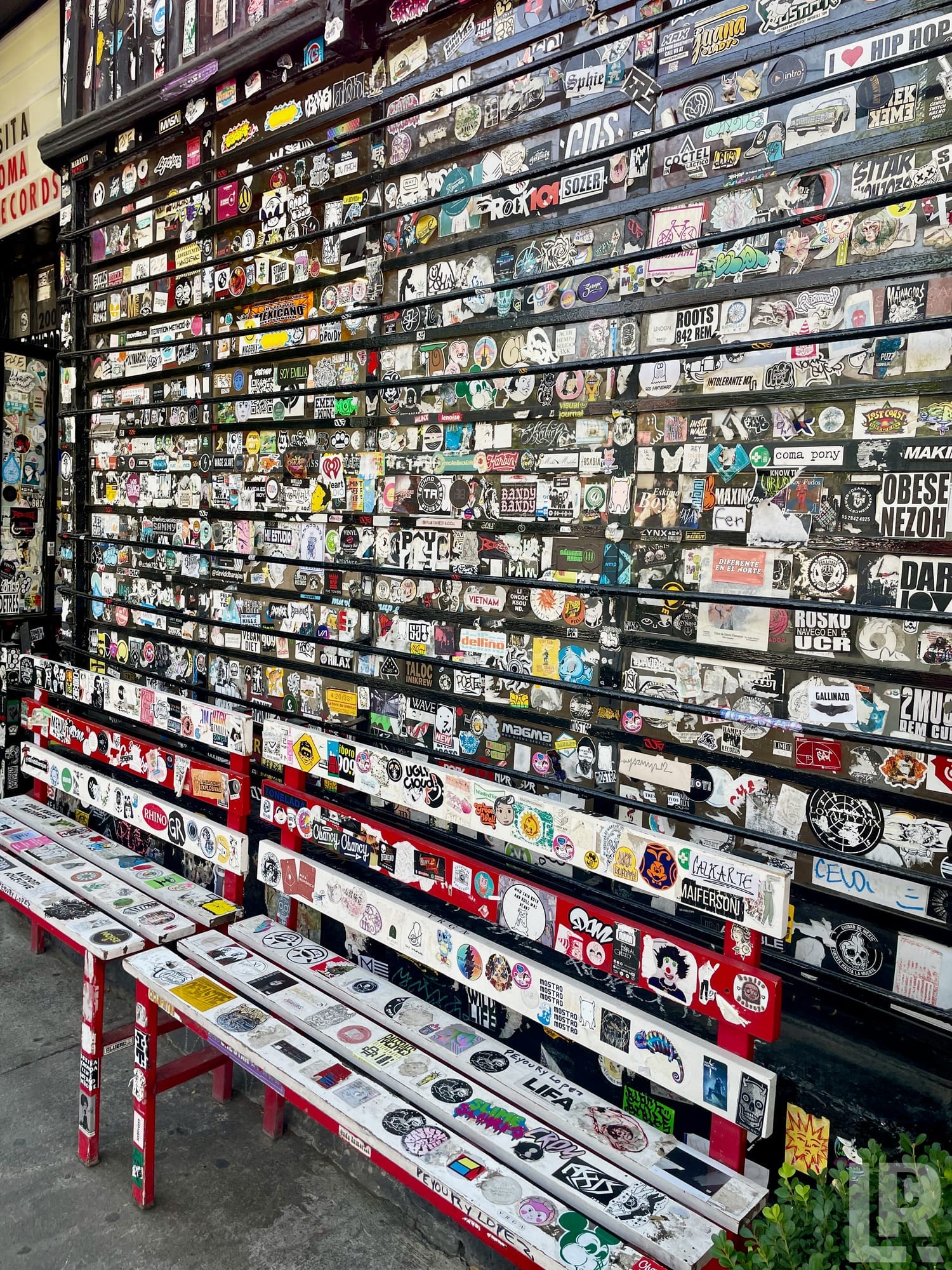 Wall and benches plastered with colorful stickers outside a record store