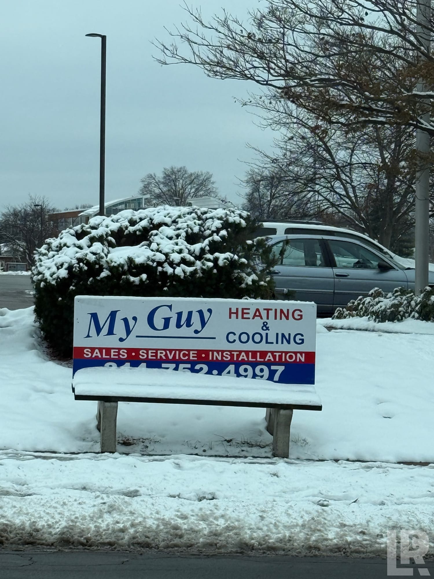 Sign reading My Guy Heating and Cooling with phone number, surrounded by snow