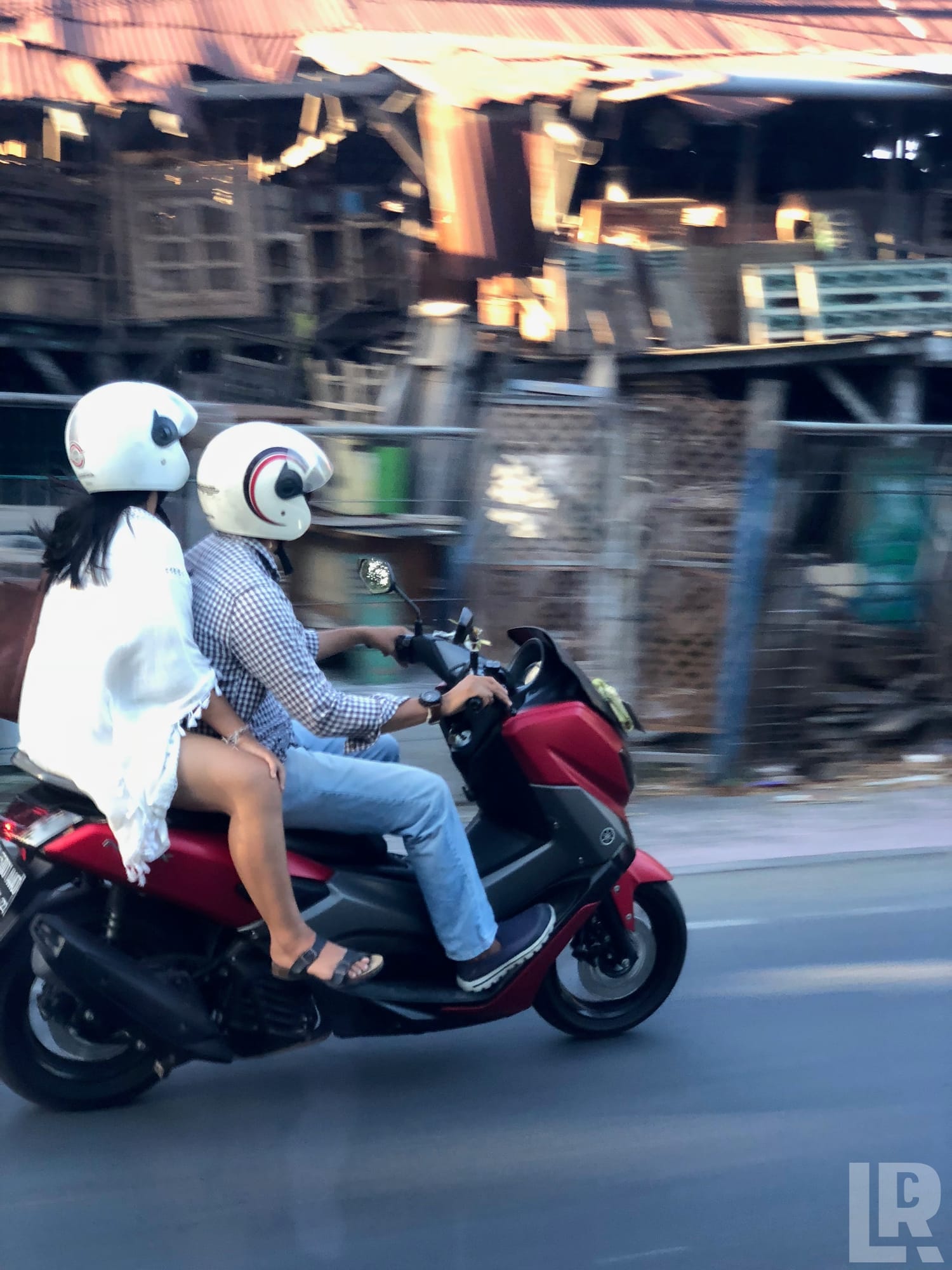 Two helmeted riders on a red Yamaha scooter moving along a road