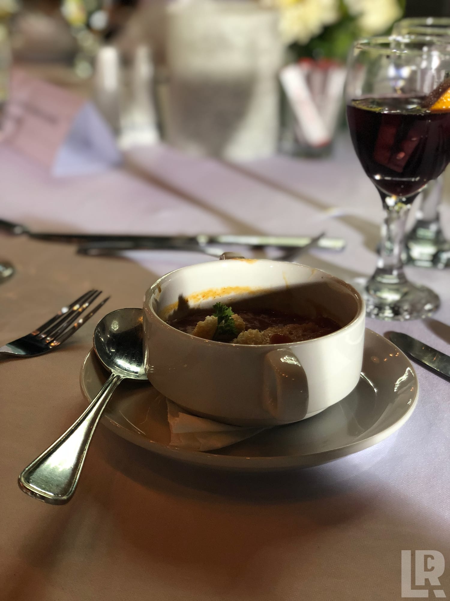 Bowl of French onion soup with melted cheese on a formal restaurant table setting with red wine