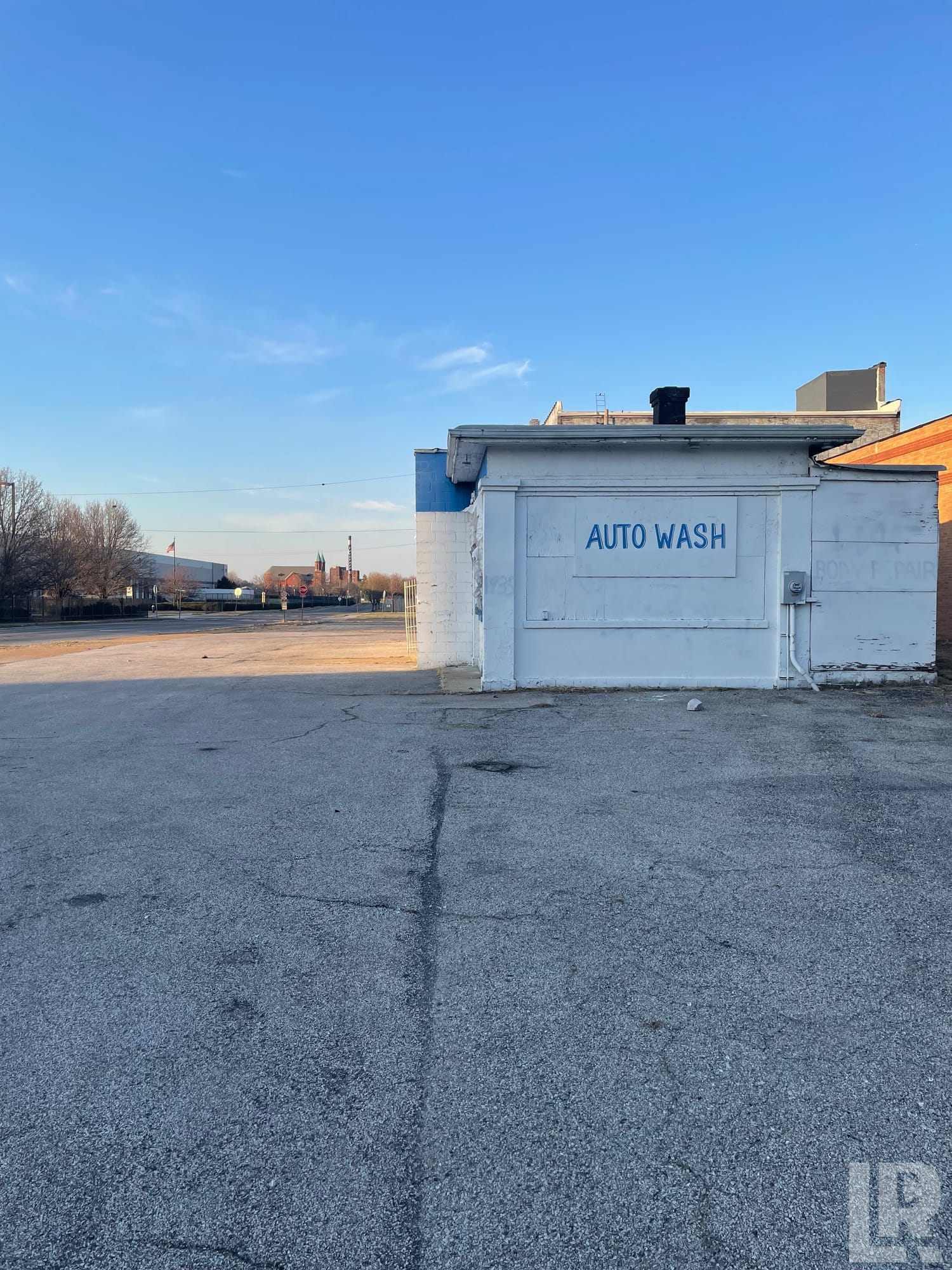 Abandoned auto wash building with painted blue sign on white exterior wall next to empty cracked parking lot