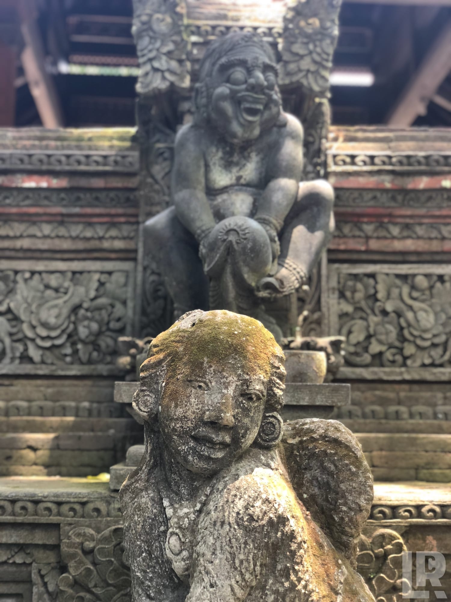 Moss-covered Balinese stone statues on a carved temple wall