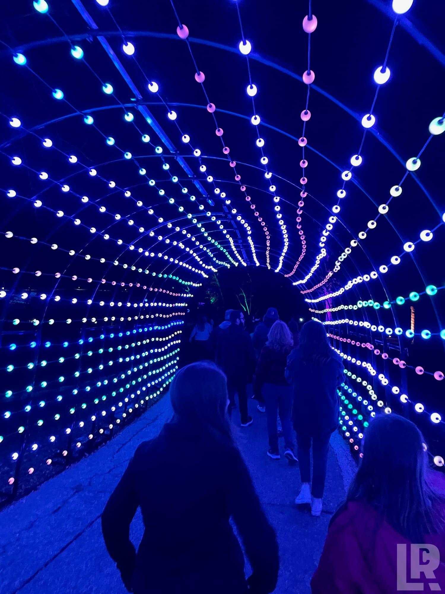 People walking through a colorful illuminated LED tunnel at night