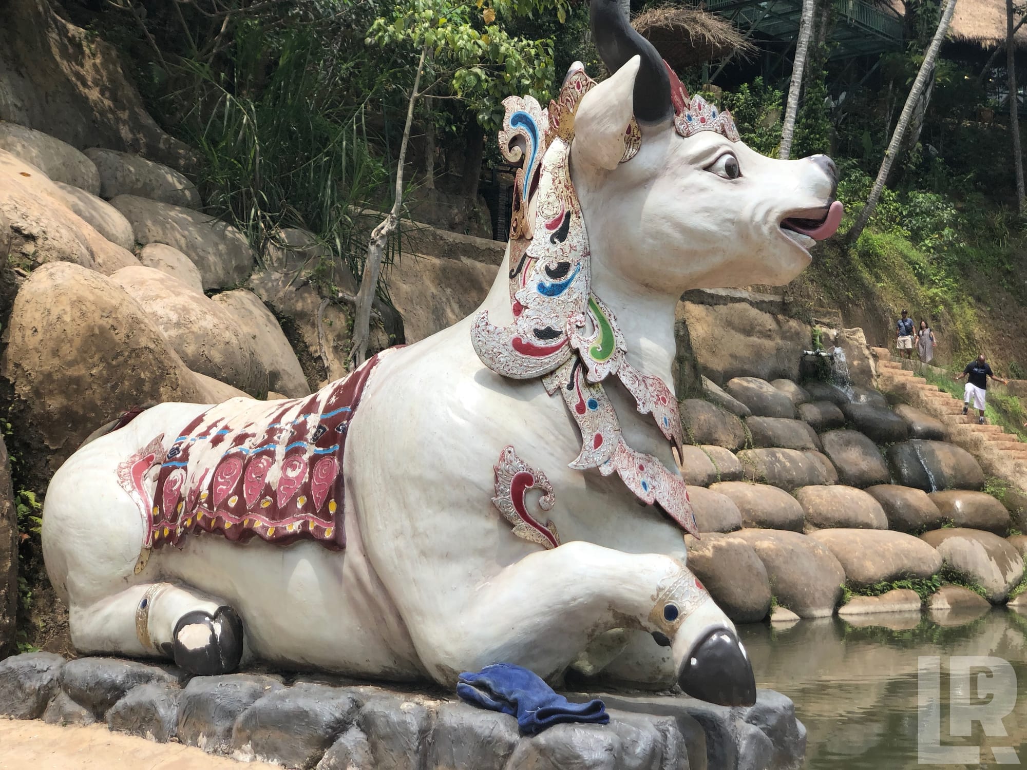 Large decorative white bull statue with colorful traditional ornamentation beside a pool in a tropical setting
