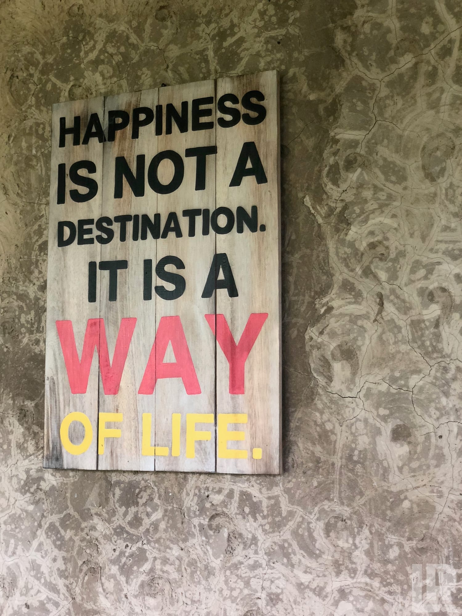 Wooden sign reading Happiness is not a destination it is a way of life on a textured stucco wall
