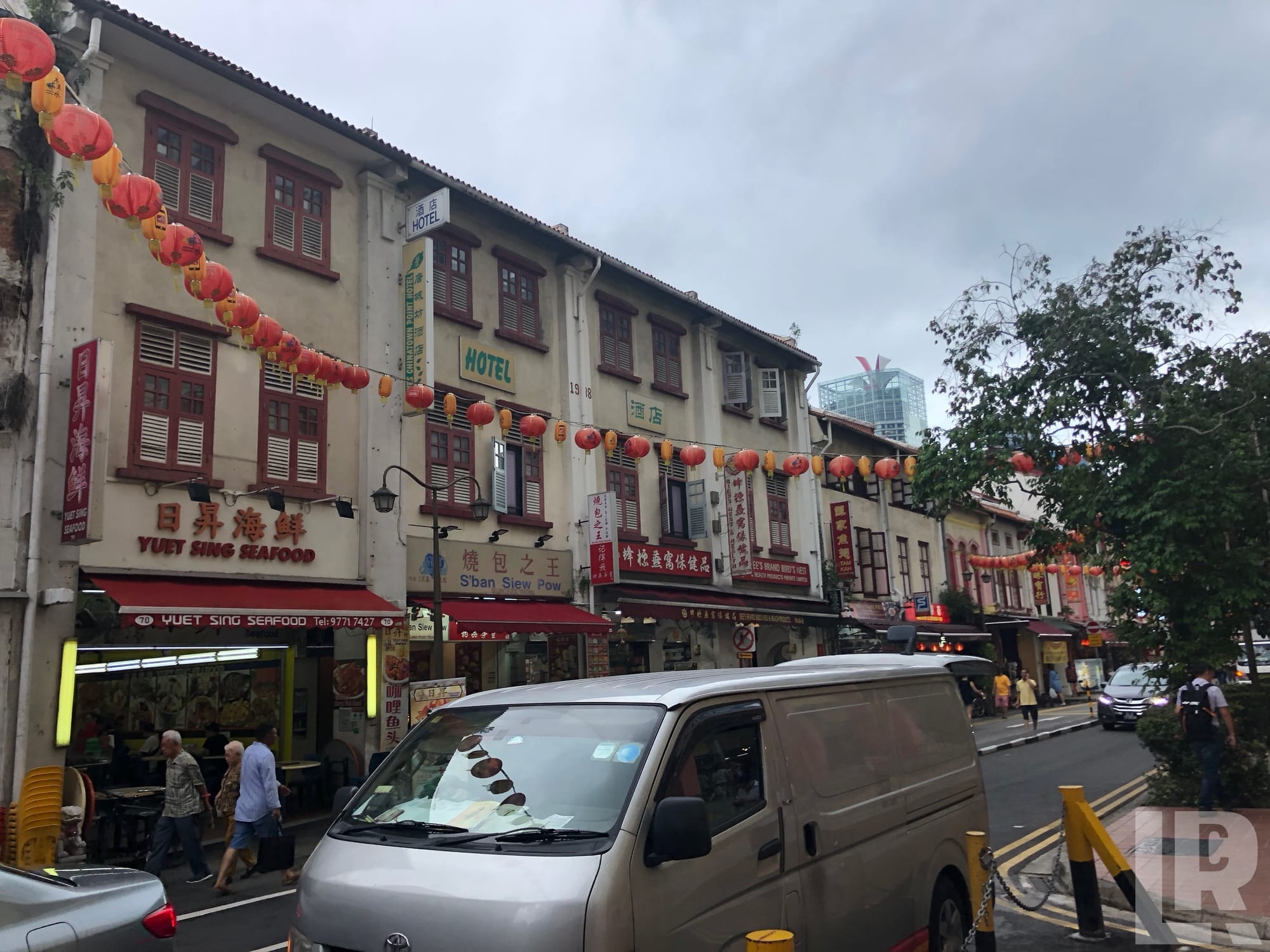 Chinatown street with red lanterns hanging between colonial shophouses and a hotel sign
