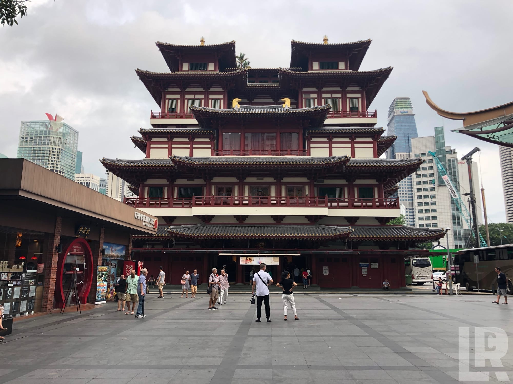 Multi-tiered red pagoda temple with tourists in foreground and city skyscrapers behind