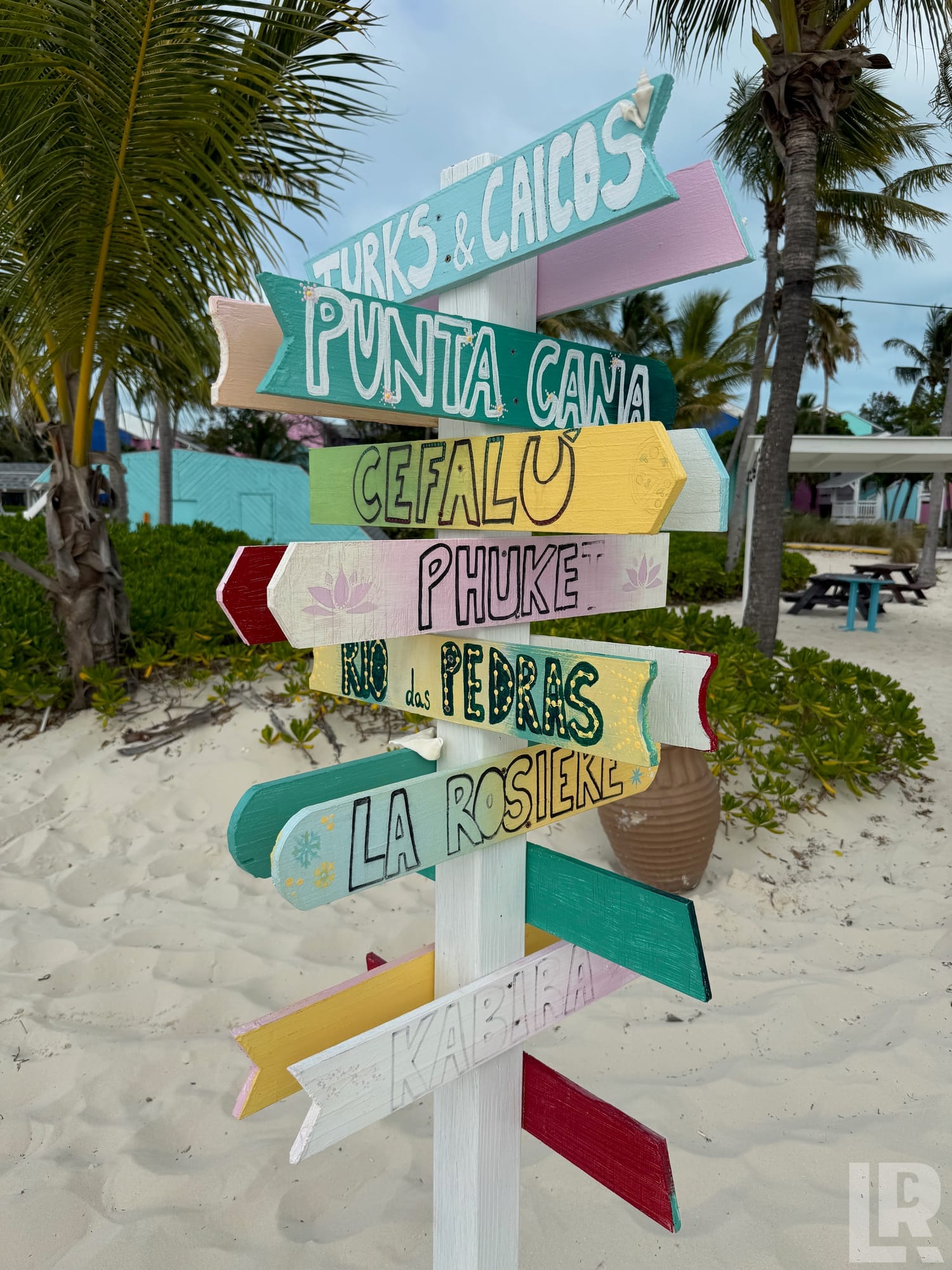 Colorful painted wooden directional signs on a beach post pointing to multiple tropical destinations