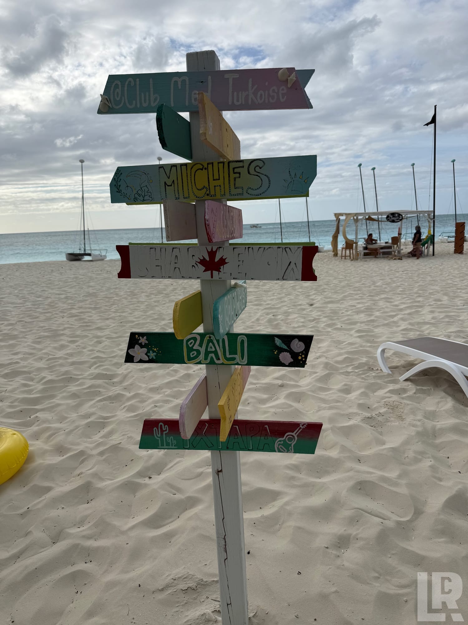Colorful multi-directional wooden beach signpost with destination names on a sandy beach