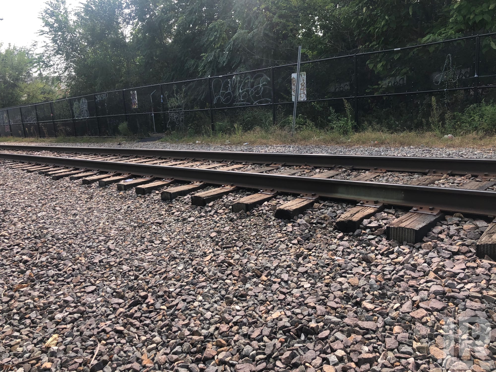 Railroad track with gravel and wooden ties next to a graffiti-covered chain-link fence