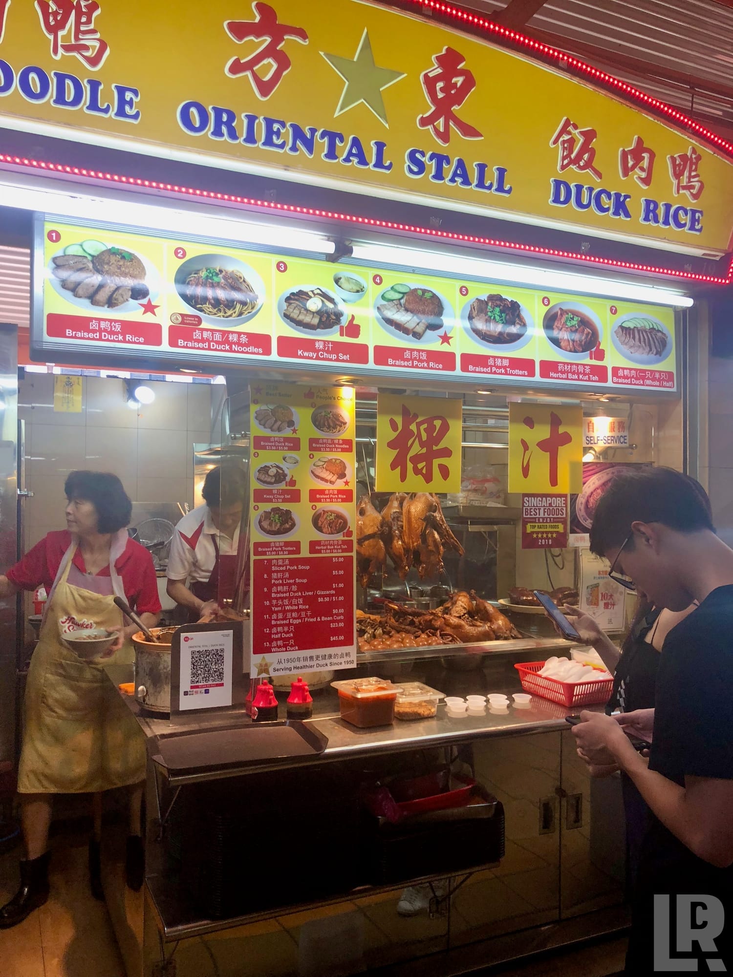 Colorful Singapore hawker stall selling duck rice and braised noodles with menu photos displayed above the counter