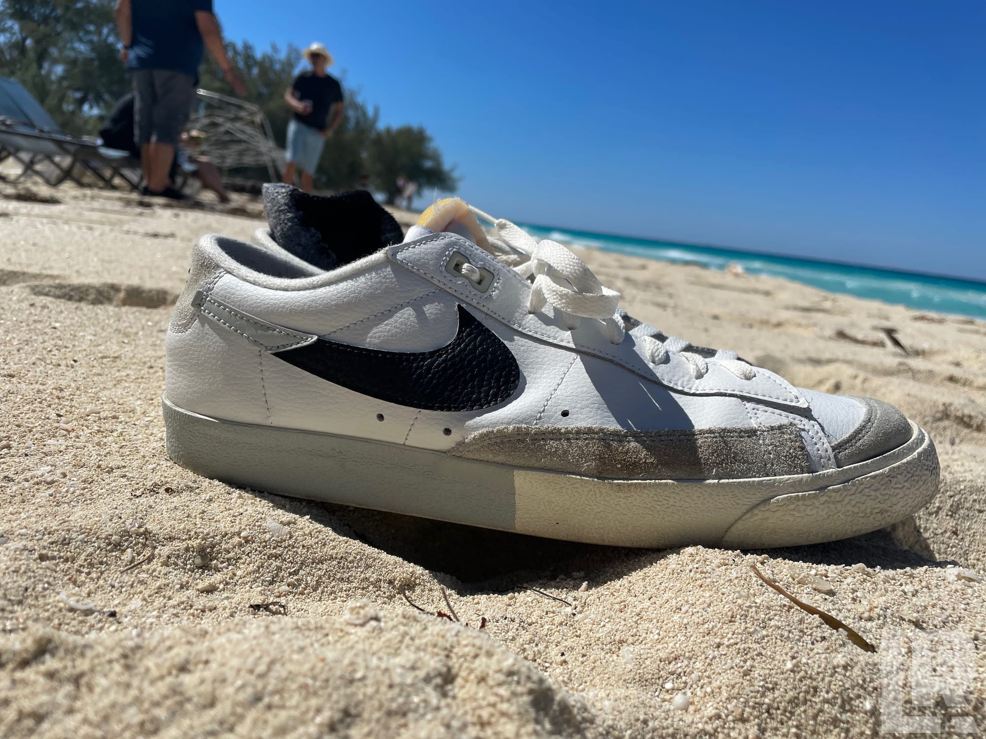 White Nike Blazer sneaker resting on sand at a sunny beach