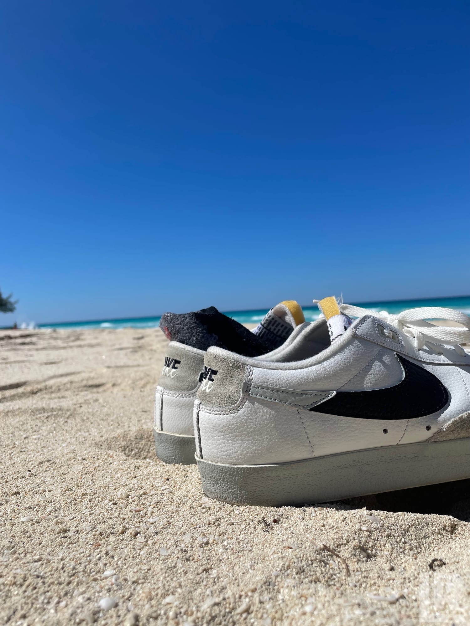 White Nike sneakers placed on a sandy beach with blue ocean and clear sky behind them