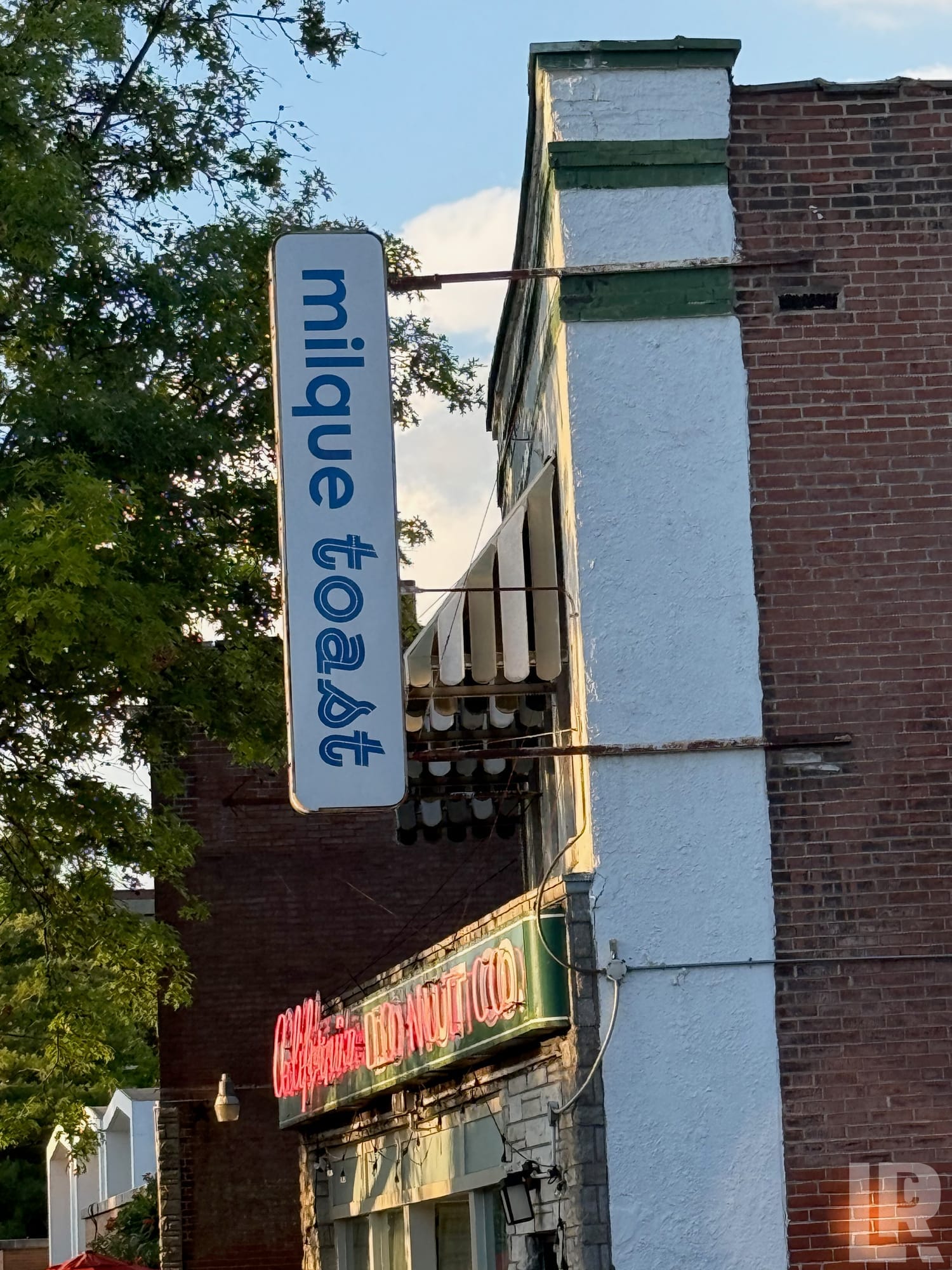 Vertical sign for Mique Toast restaurant on a brick building corner with a donut shop sign below